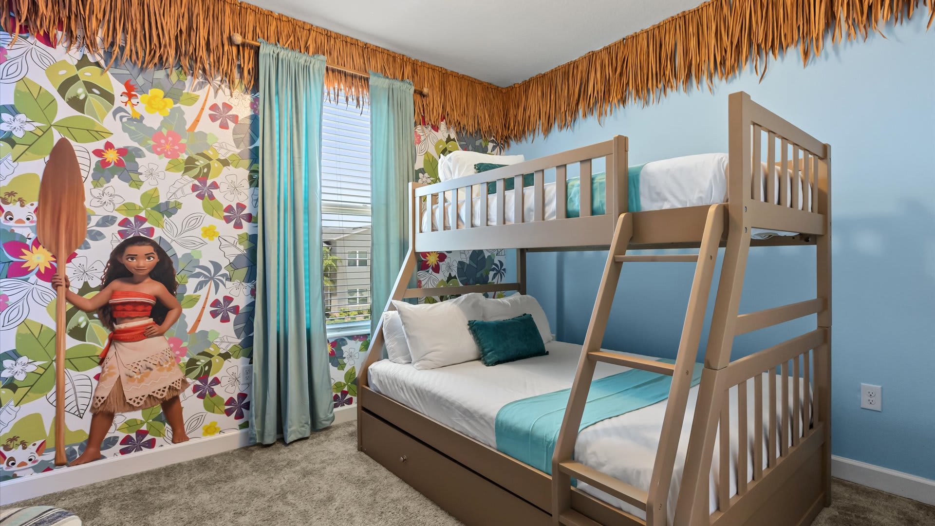 Vibrant Moana-themed bedroom with a light wood bunk bed (full over twin with trundle), a colorful mural of Moana on one wall, and light blue walls. A window with blue curtains provides natural light.