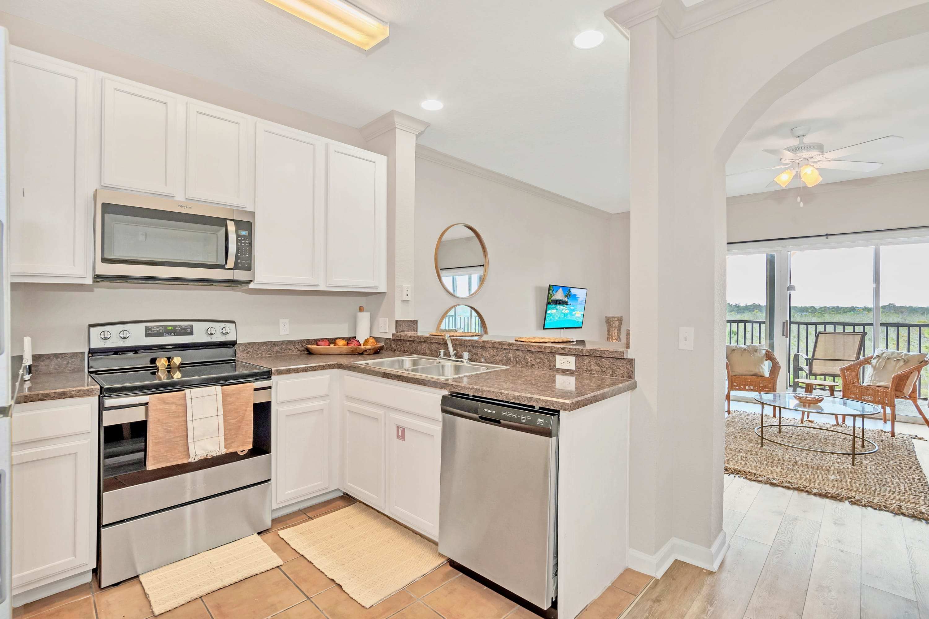 Kitchen with white cabinets and dark countertops, stainless steel appliances, and a tiled floor, offering a view into the living area and a balcony with outdoor seating.