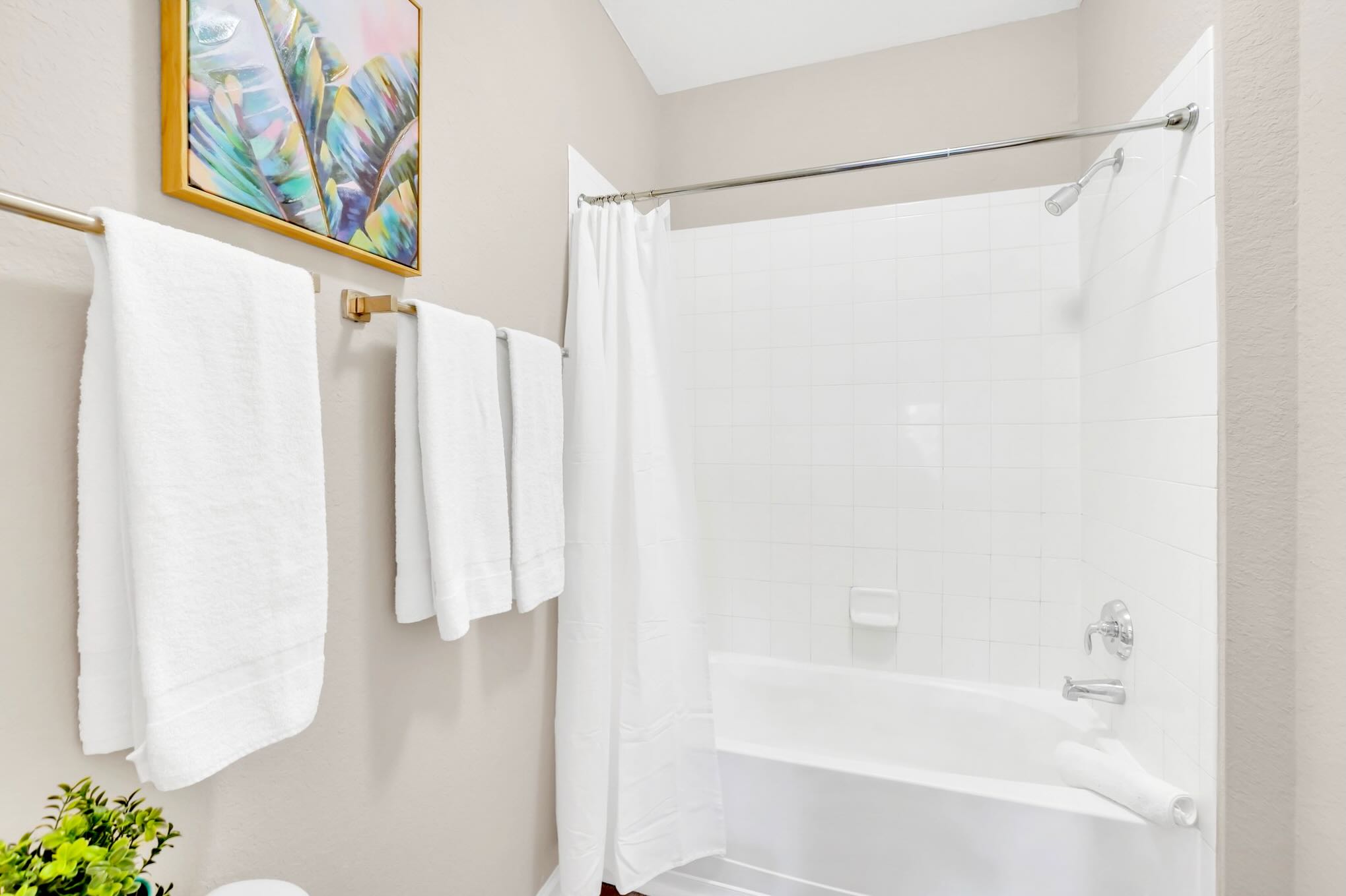 A clean bathroom featuring a white shower/tub combo with a white tile surround and a shower curtain, complemented by a towel rack with fresh white towels.