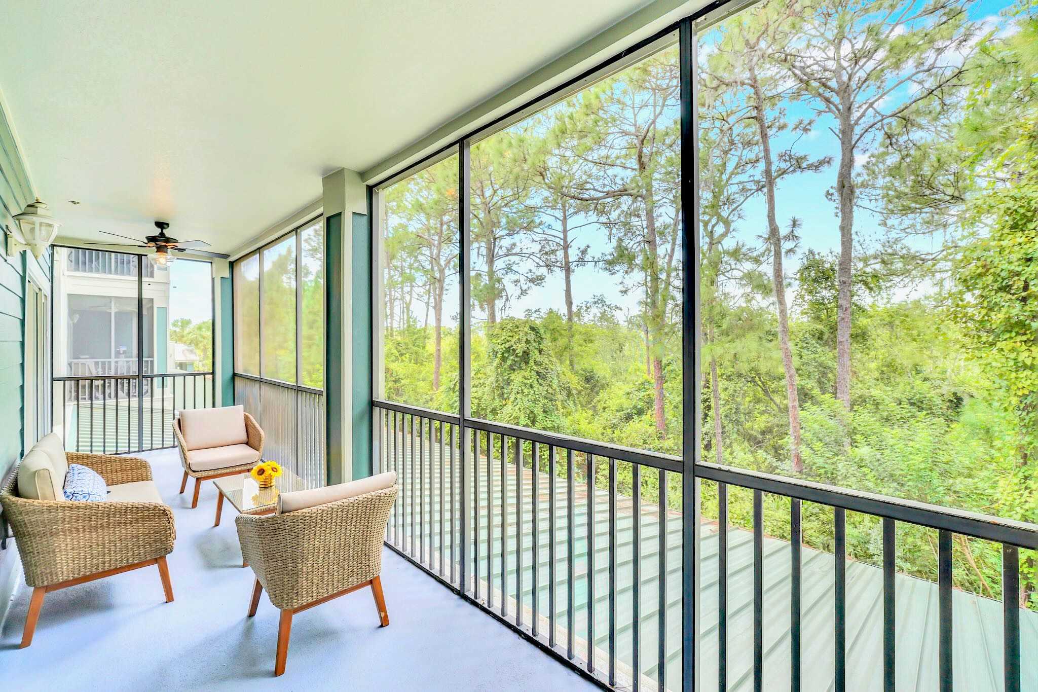 Expansive screened balcony providing panoramic views of dense green trees and foliage, furnished with comfortable wicker seating for outdoor relaxation.