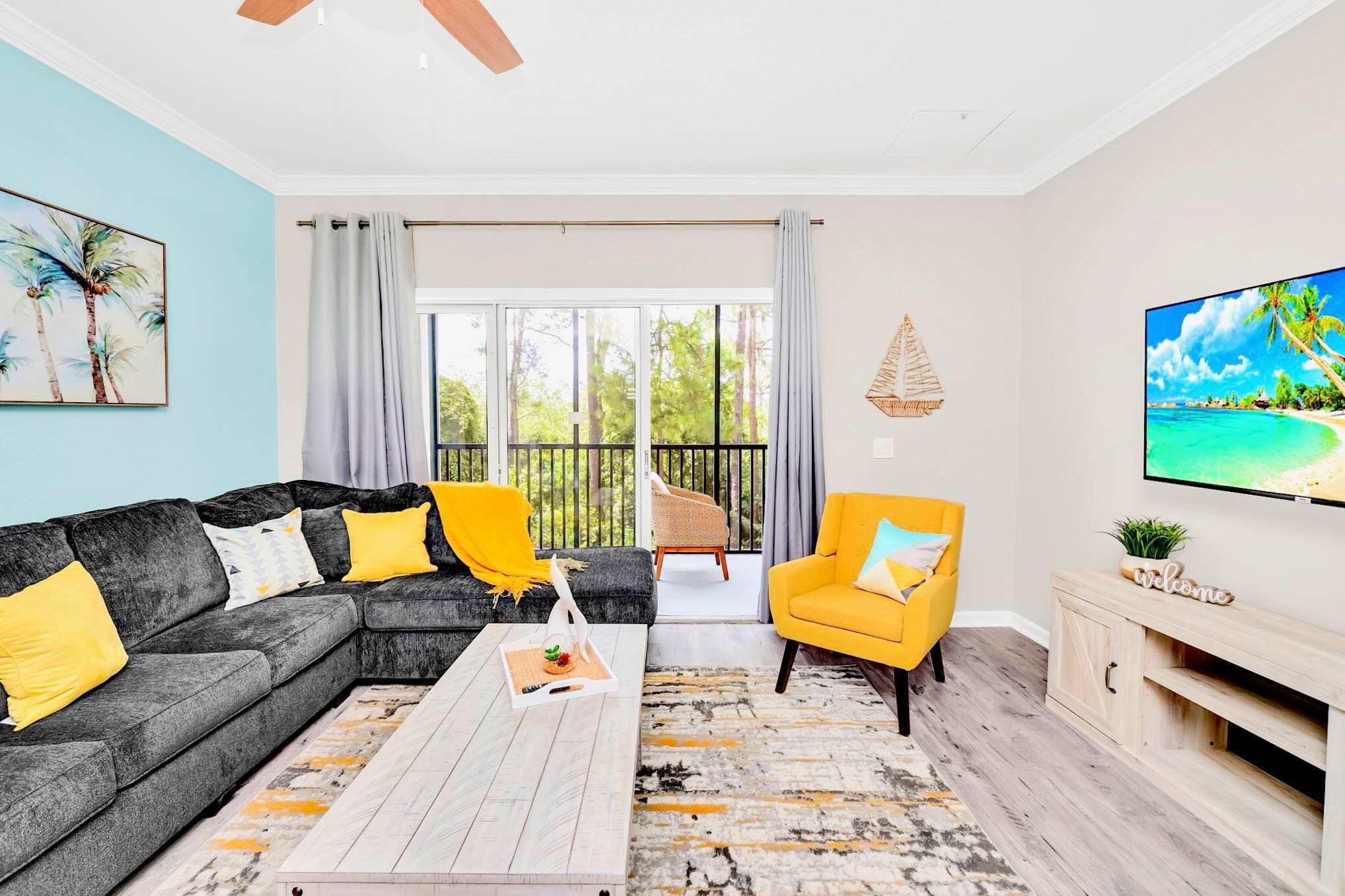 Inviting living room featuring a large gray sectional sofa, a vibrant yellow accent armchair, a light wood coffee table, and a wall-mounted TV, with access to a screened balcony.