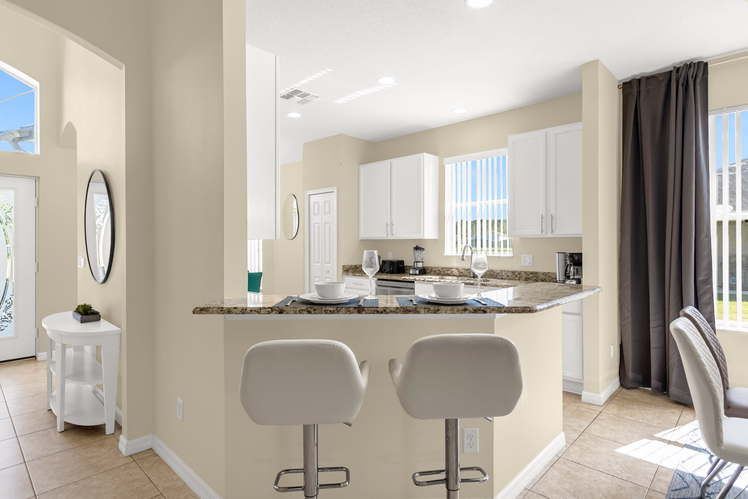 A kitchen island with a granite countertop and two white upholstered bar stools, offering a casual dining spot, with white cabinets and a window visible in the background.