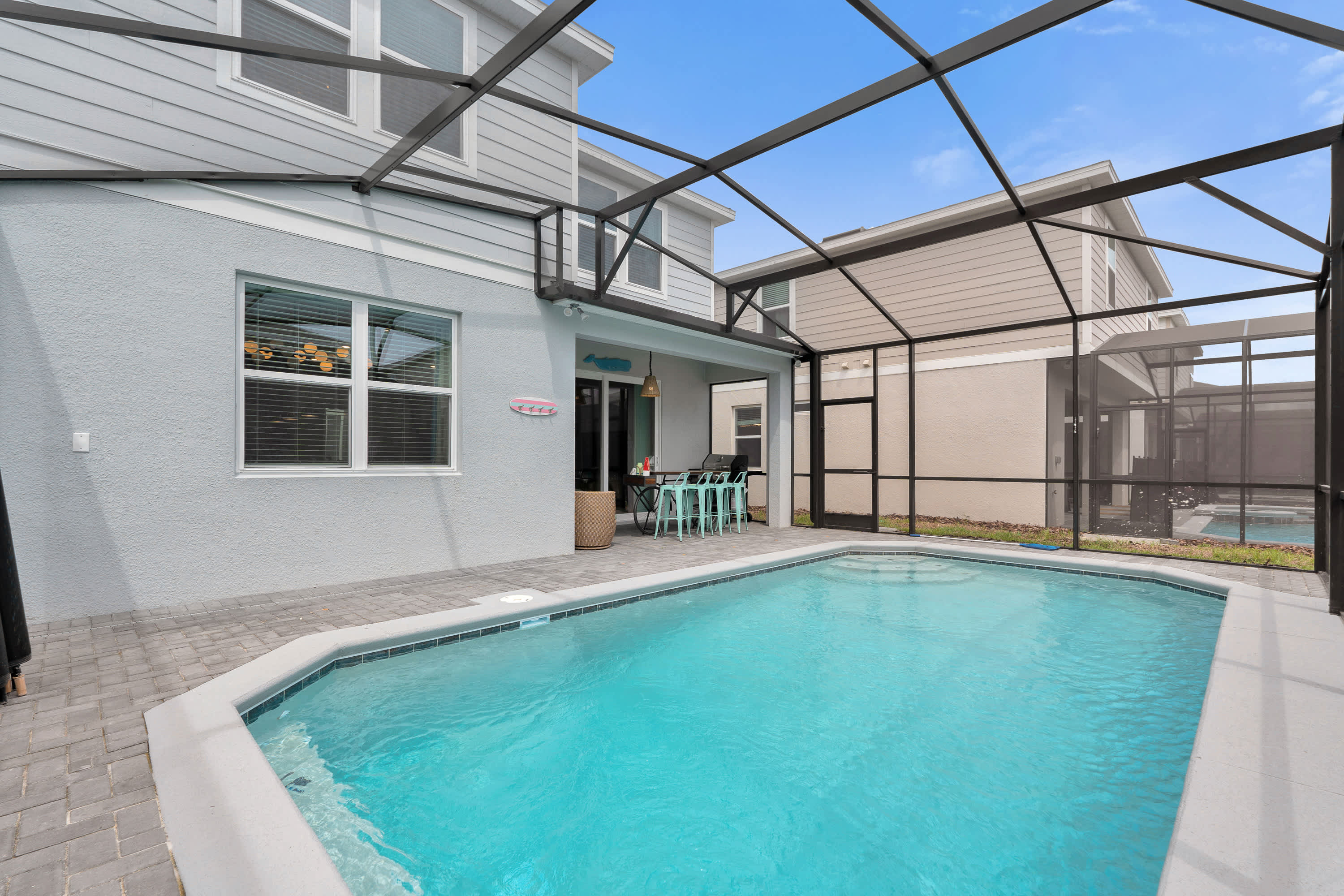 The private swimming pool and screened patio area, showing the back of the house with multiple windows and a sliding glass door, under a bright blue sky.