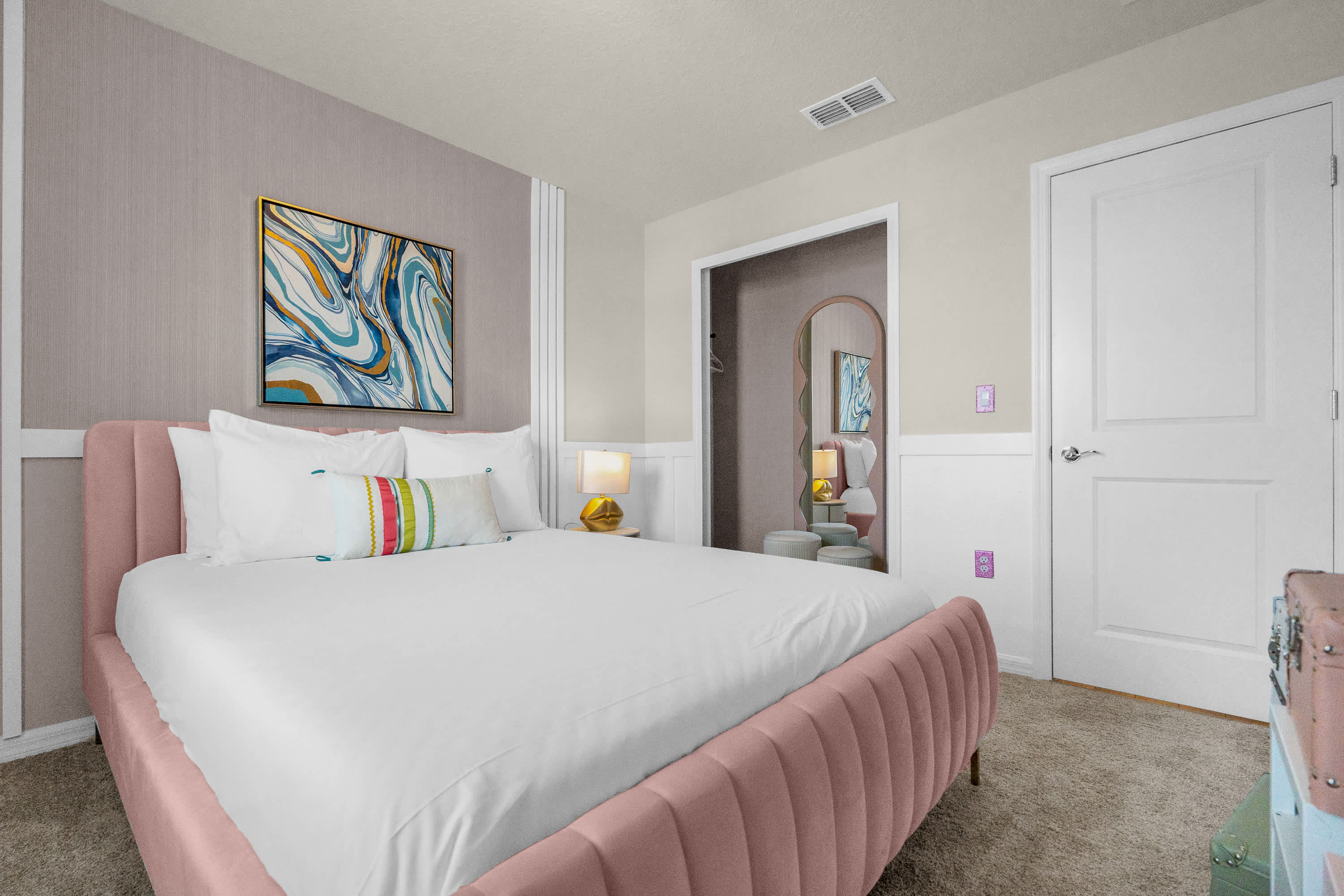 Another angle of the pink-themed bedroom, highlighting the bed, a large abstract artwork above the headboard, and a full-length arched mirror visible through an open doorway, adding depth to the space.