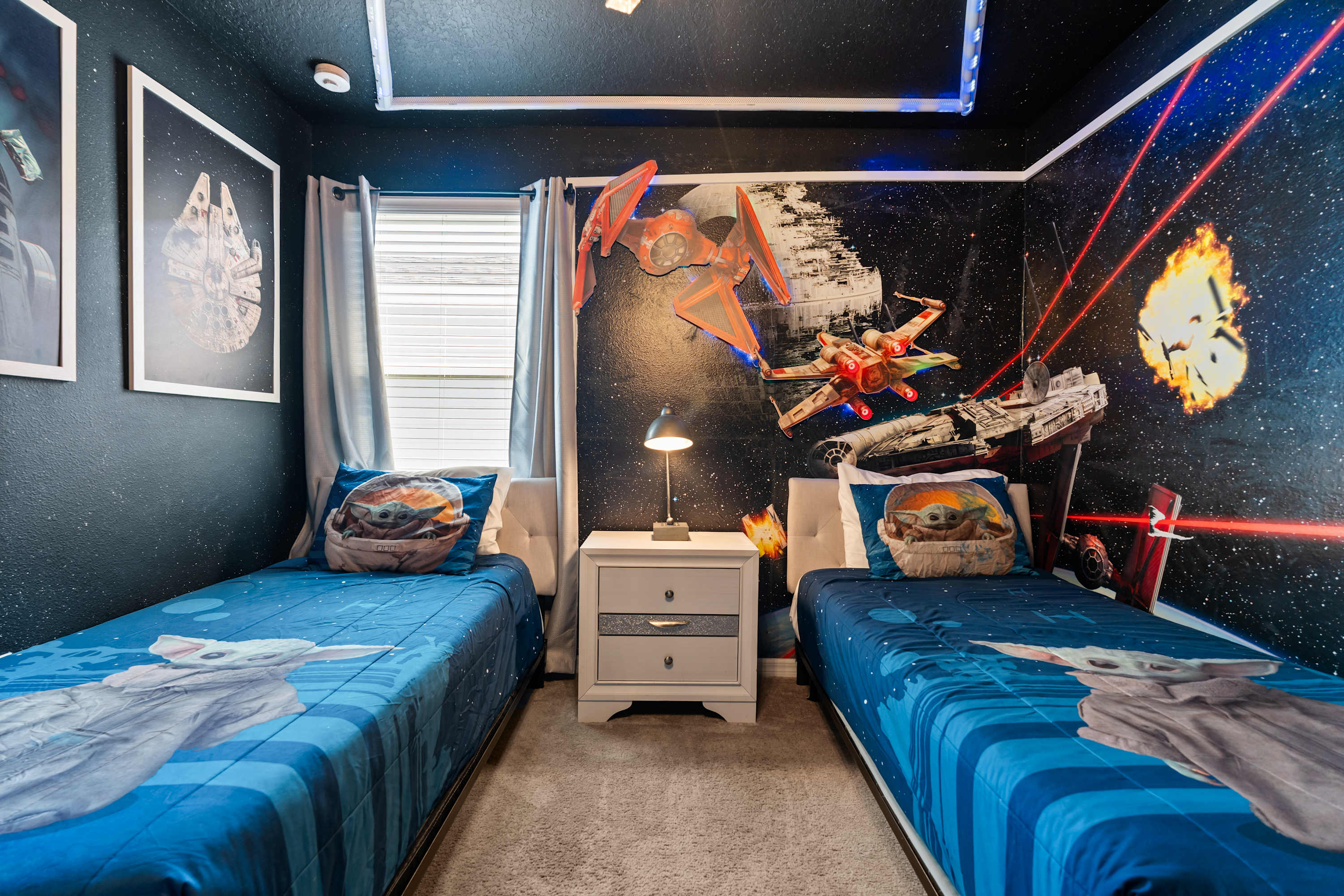 A close-up view of the Star Wars-themed bedroom shows two twin beds with Grogu bedding, a shared nightstand with a lamp, and a detailed wall mural with 3D spaceship elements and laser effects.