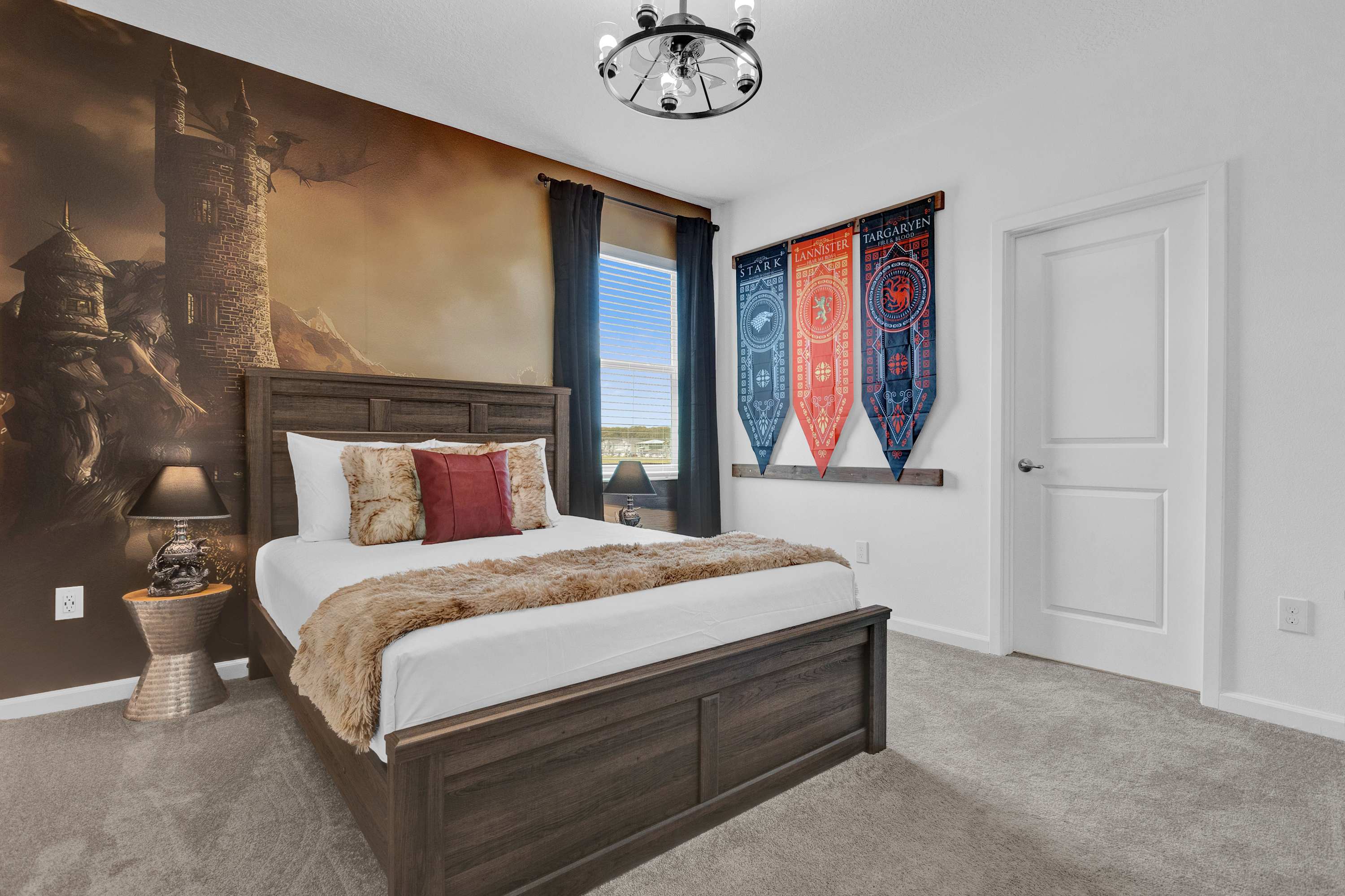 A "Game of Thrones" themed bedroom featuring a dark wood queen-sized bed with a faux fur throw, a dramatic castle mural on one wall, and decorative house banners, creating a medieval fantasy ambiance.