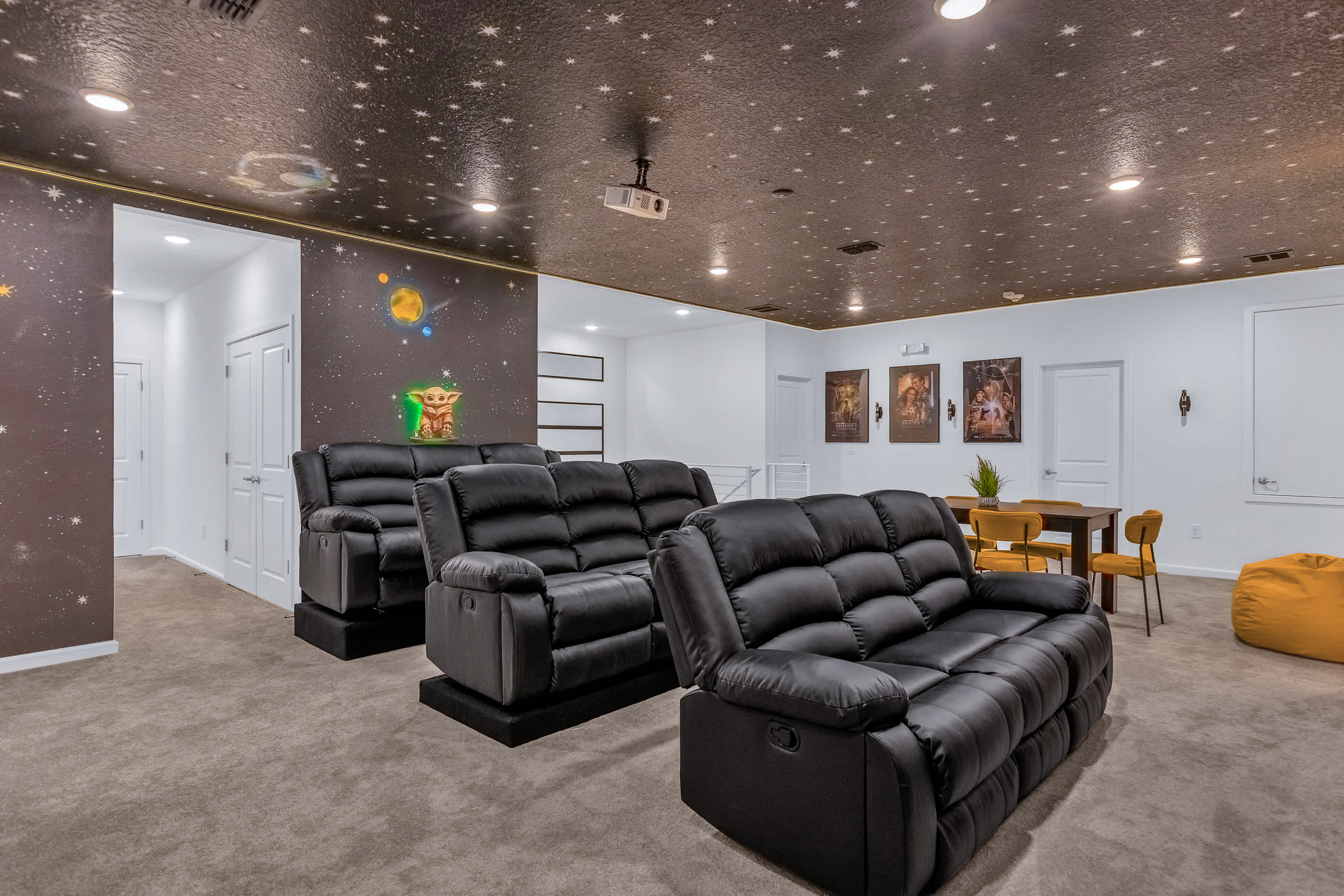 Expansive media room with multiple rows of black reclining sofas facing a projection screen (not fully visible). The walls feature Star Wars murals, including Grogu, and the ceiling is dark with numerous star-like lights.