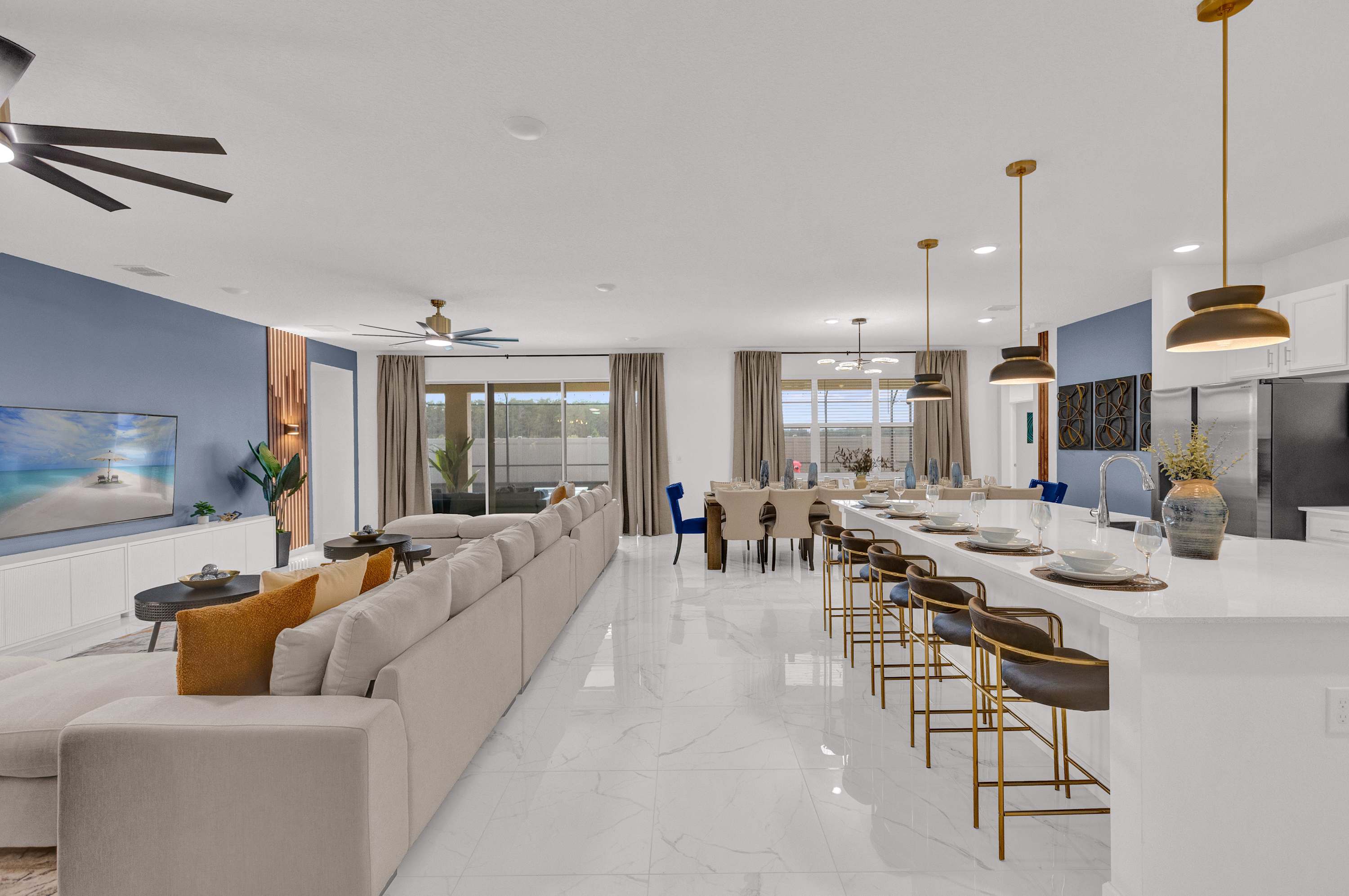 A spacious open-concept living area with white tiled floors, a large L-shaped beige sectional sofa, a dining area with a long table, and a modern kitchen with white cabinets and a large island with bar stools.