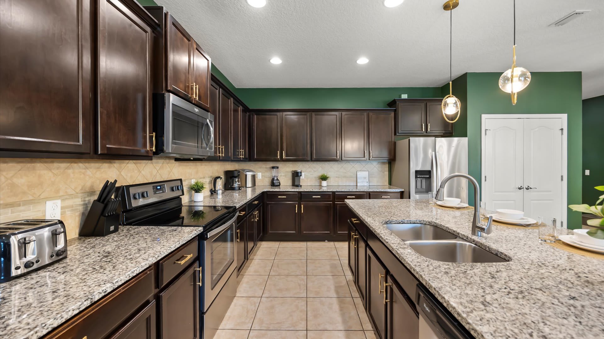 Modern kitchen with dark wood cabinetry, light granite countertops, and a large island with a double sink, set against a vibrant green accent wall.
