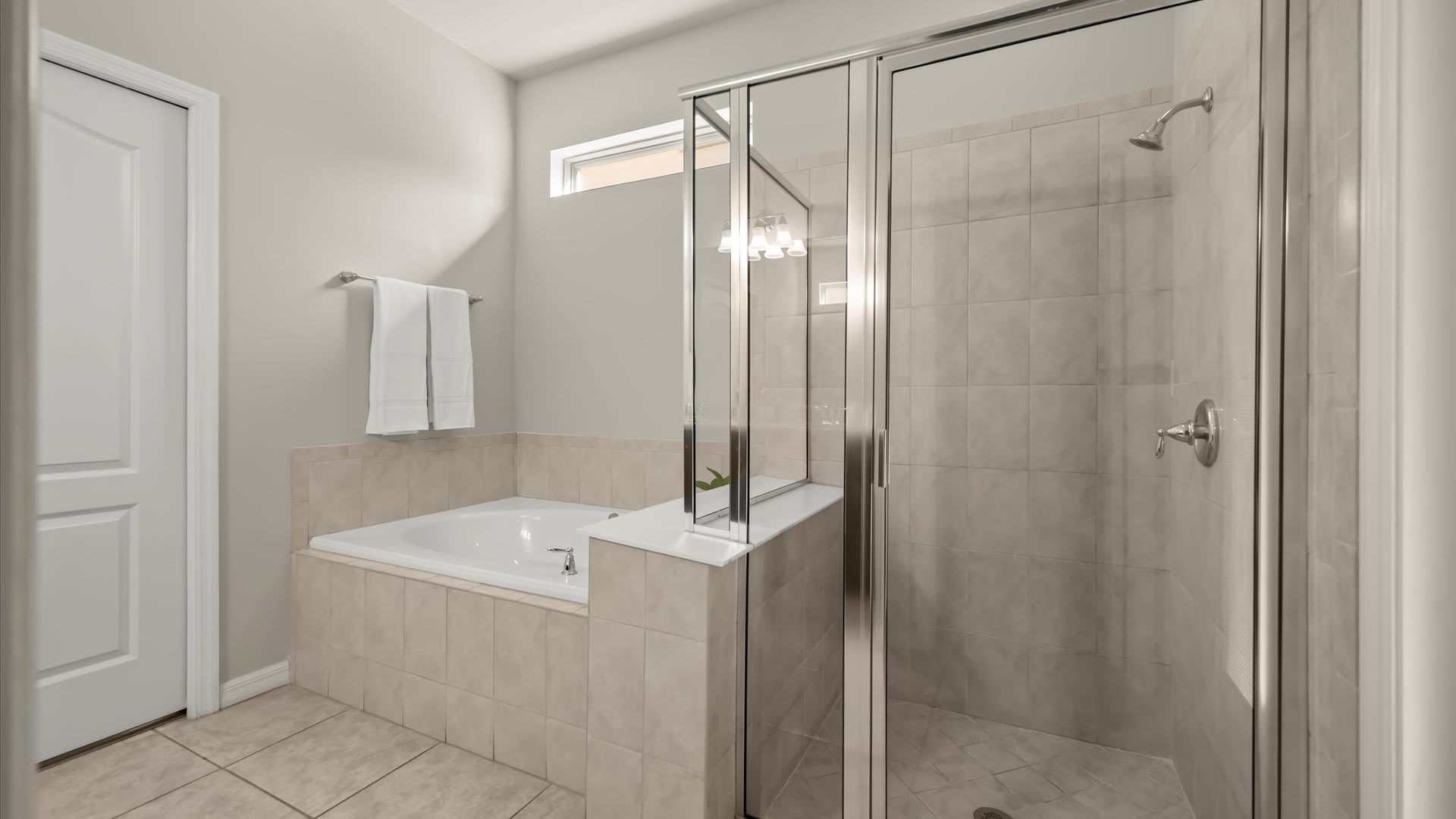 Part of the bathroom featuring a large soaking tub and a separate glass-enclosed shower with tiled walls, maintaining a neutral color palette.