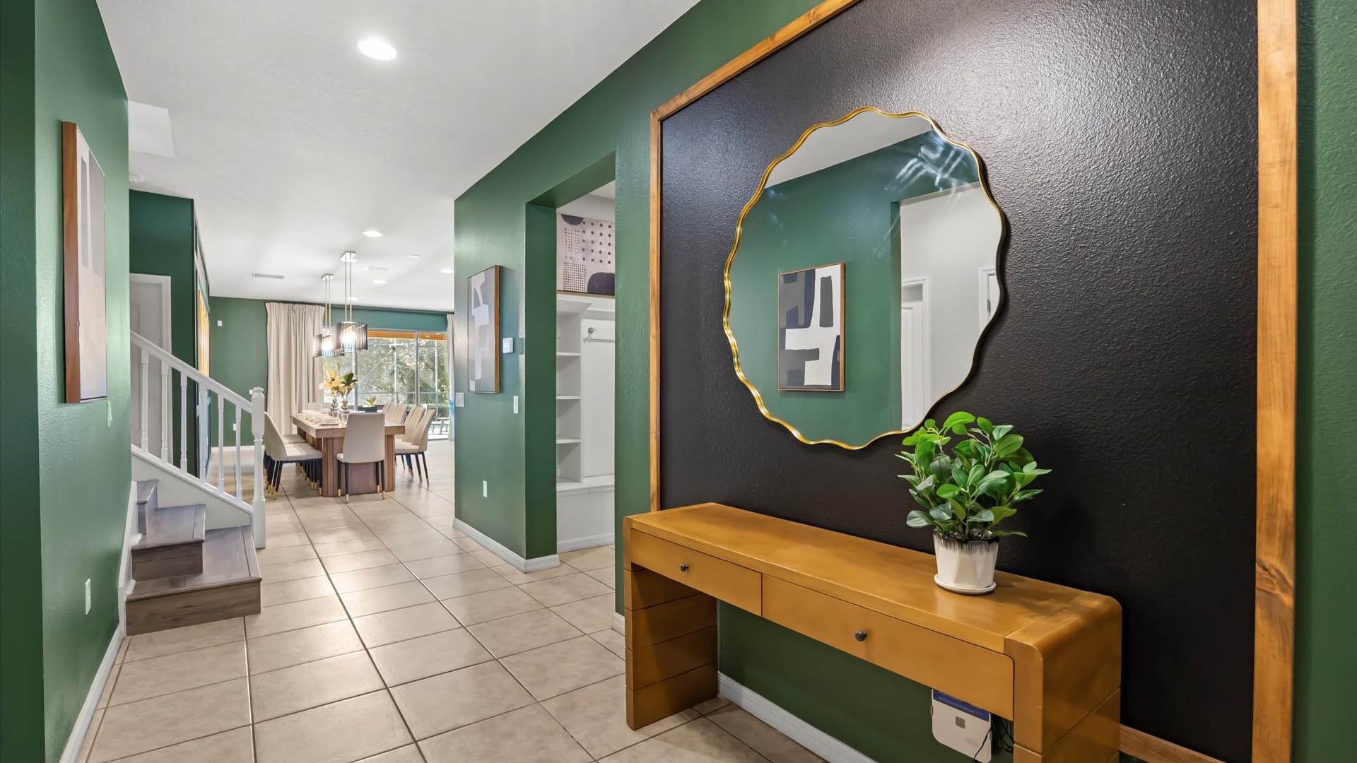 Inviting foyer with a dark accent wall featuring a large gold-framed mirror above a wooden console table, leading to a dining area and staircase.