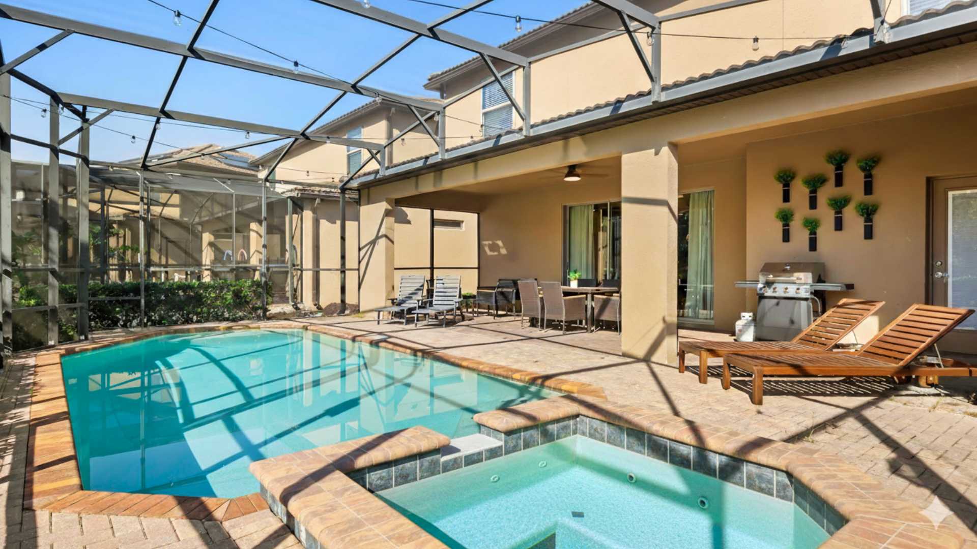 An outdoor screened-in pool area features a rectangular swimming pool with an integrated hot tub, surrounded by a brick paver deck. A covered patio with a dining table and lounge chairs is visible, along with a BBQ grill.