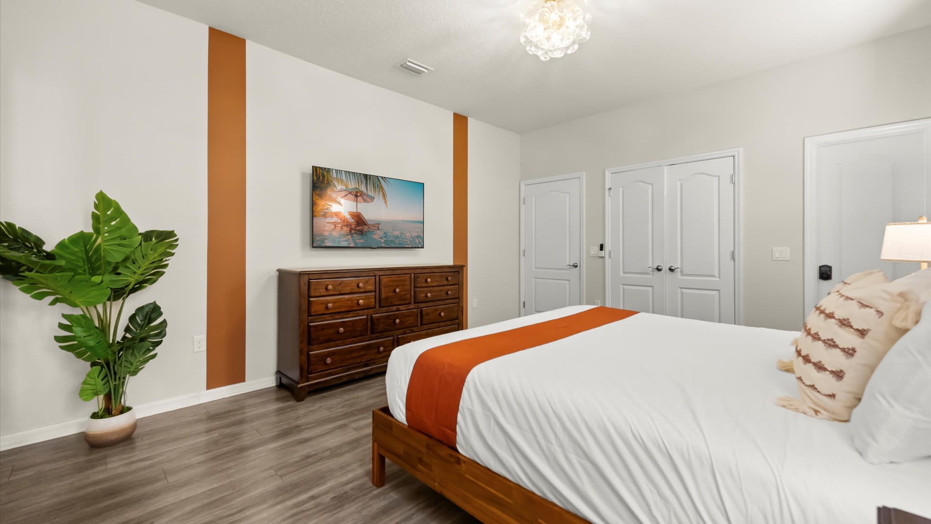 View of the same bedroom, highlighting a large wooden dresser with a wall-mounted TV above it, and a tall potted plant adding a touch of greenery.