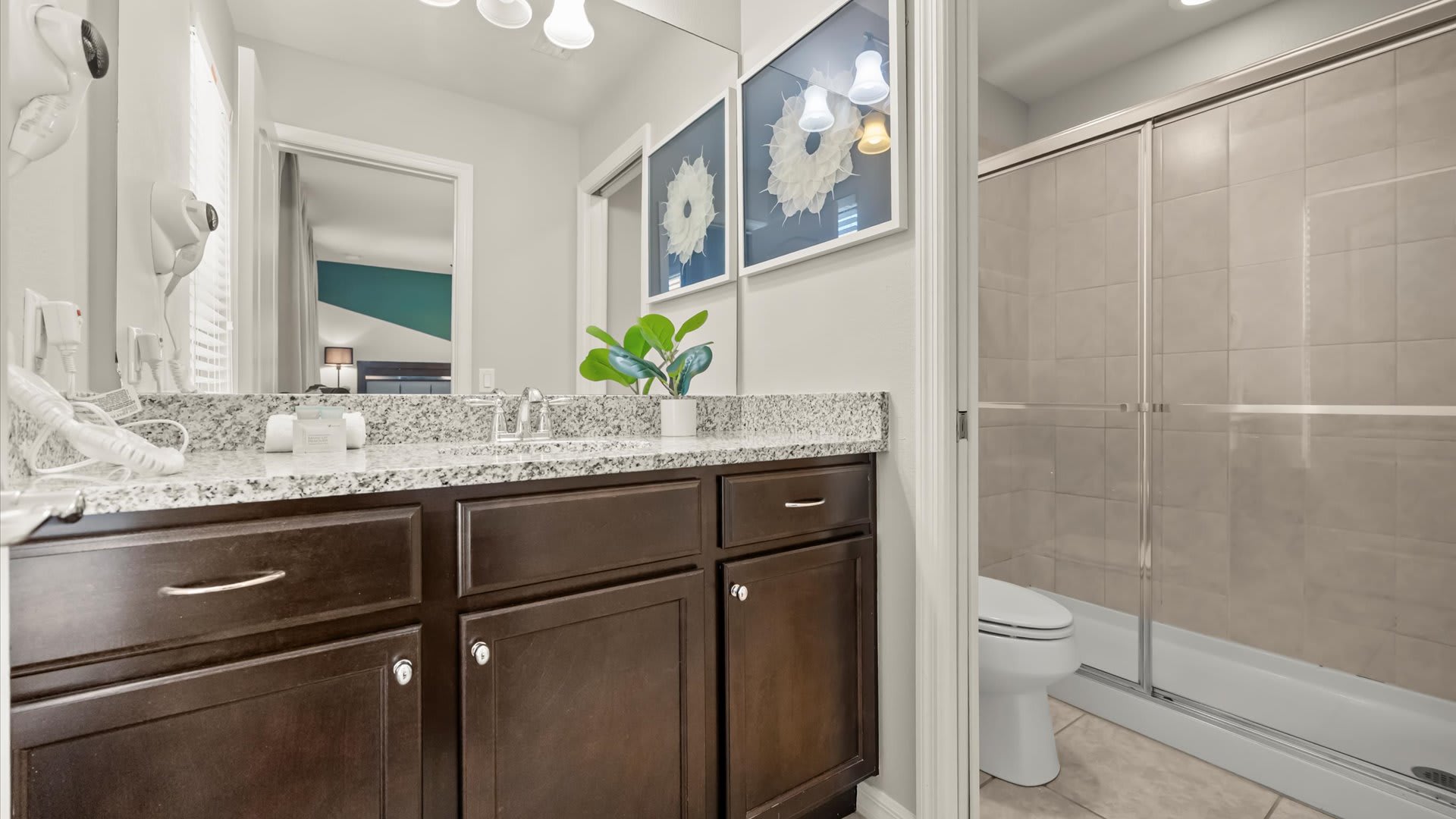A modern bathroom features a dark wood vanity with a granite countertop and single sink, a large mirror, and a walk-in shower with a glass enclosure. Light gray walls and tiled floors create a clean aesthetic.