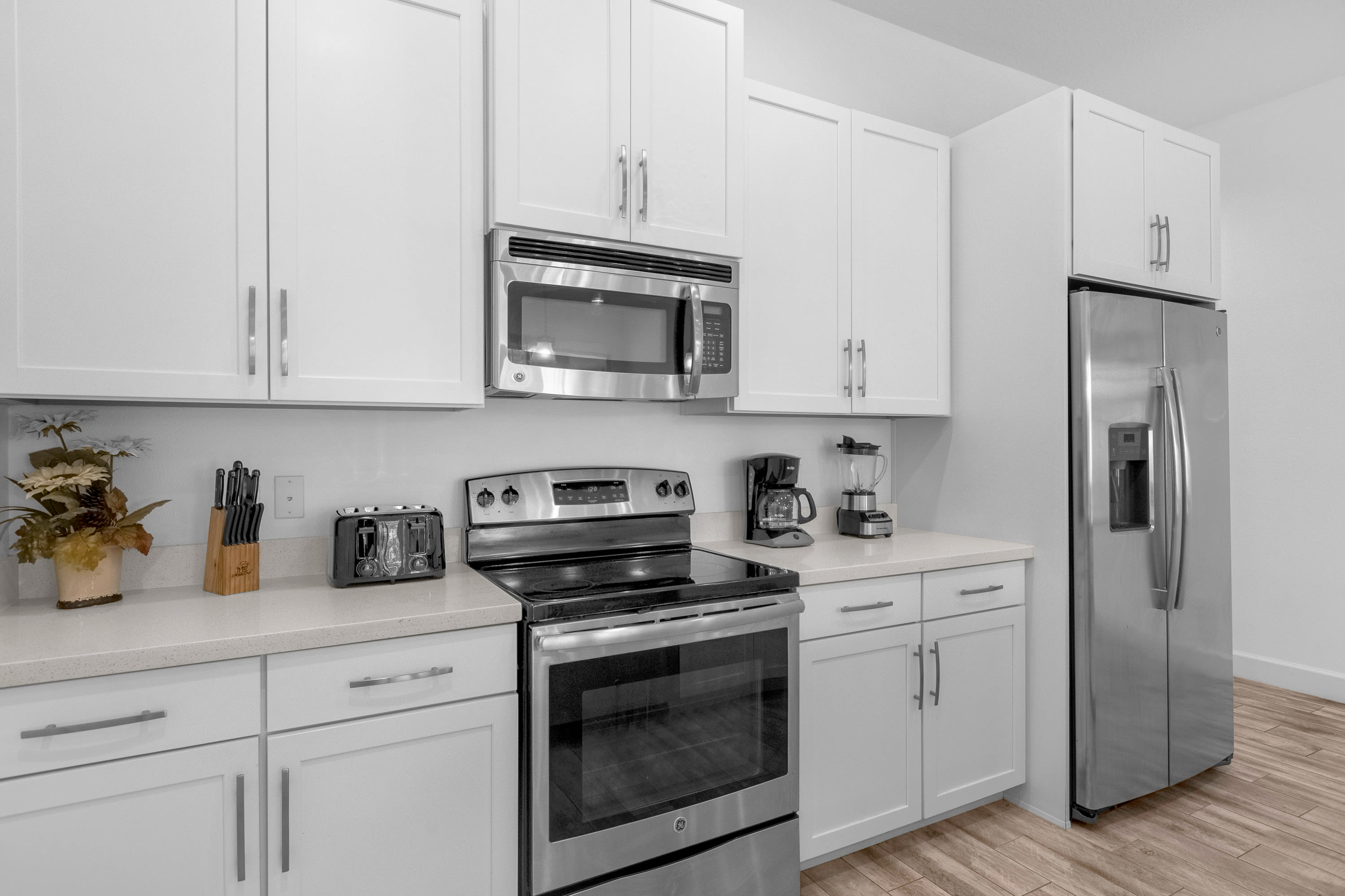 Detailed view of the kitchen counter with white shaker cabinets and light countertops, featuring a stainless steel microwave, electric range, coffee maker, and toaster. A knife block is also visible.
