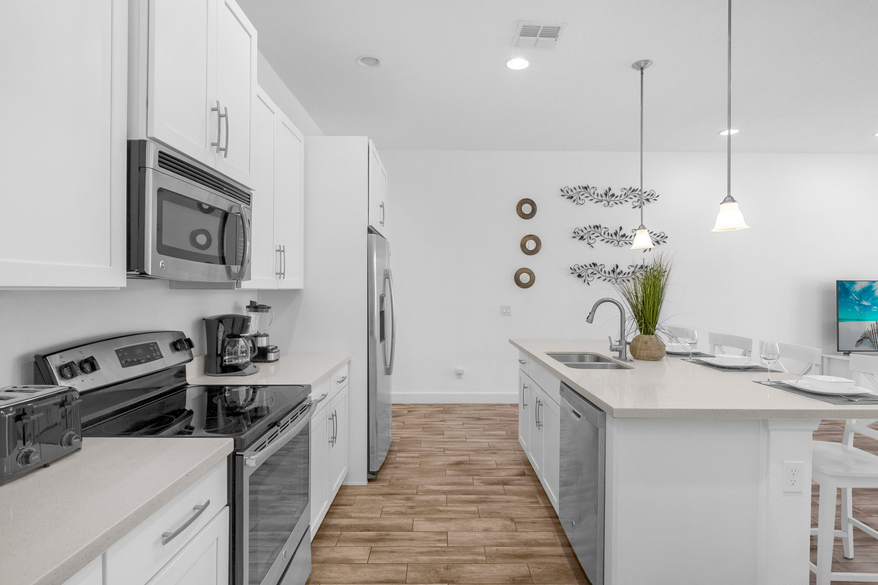 Galley-style kitchen with white shaker cabinets and light countertops, equipped with stainless steel appliances including a microwave, range, and refrigerator. A coffee maker and toaster are on the counter.