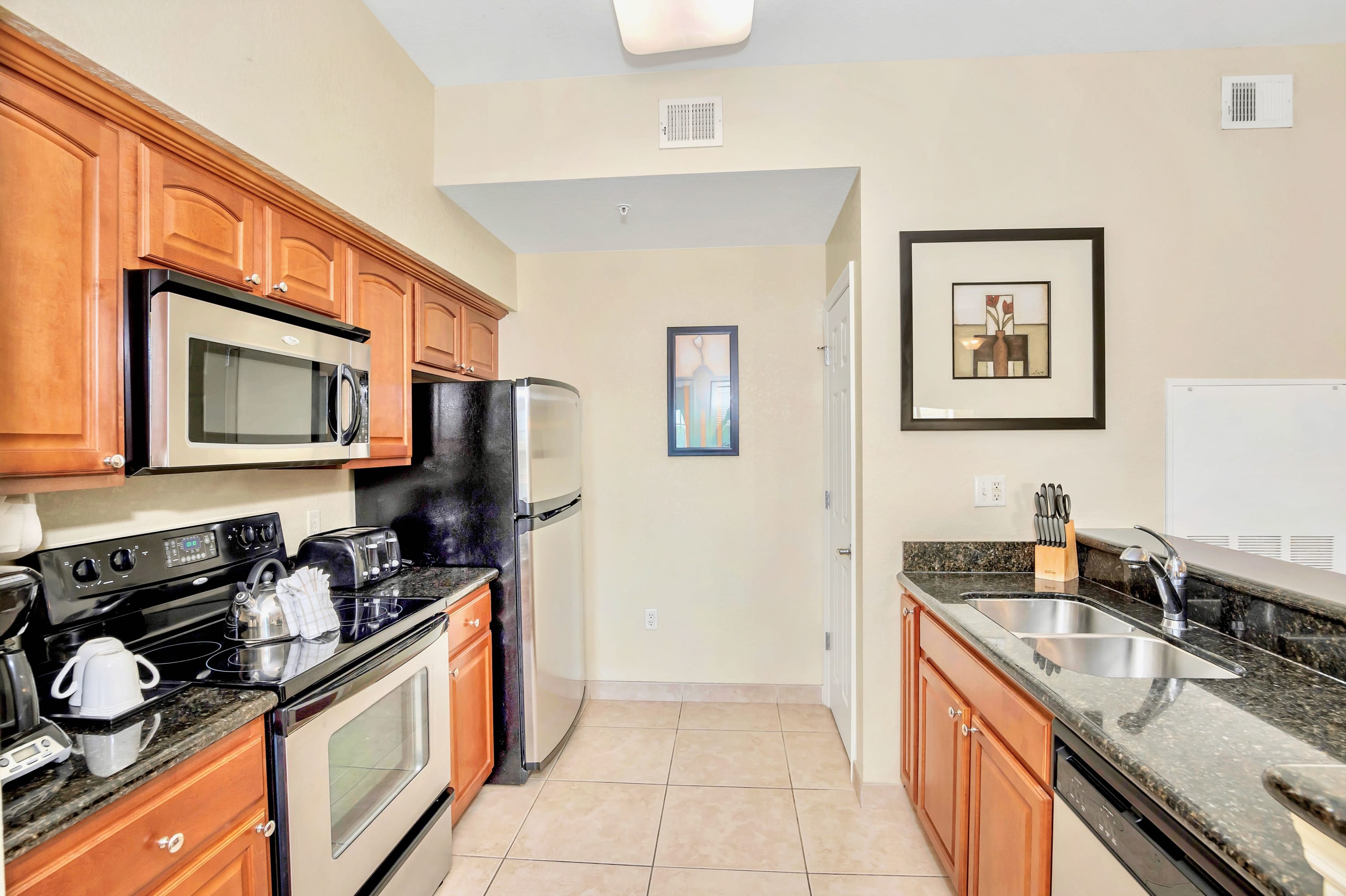View of the kitchen showcasing stainless steel appliances including a refrigerator, stove, and microwave, complemented by light wood cabinets and dark granite countertops.