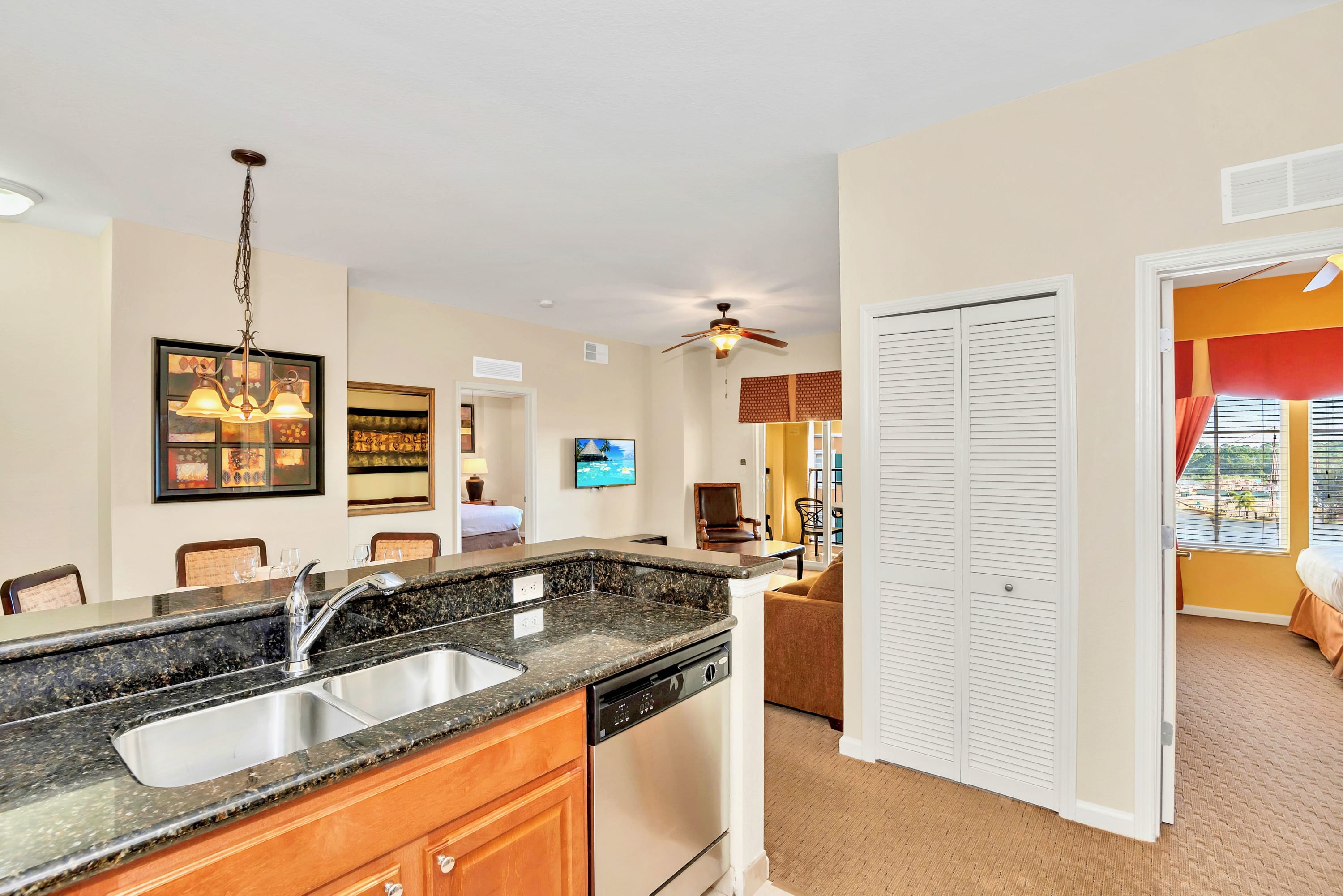 Kitchen island with a double sink and dishwasher, opening into an adjacent dining area with a table and chairs, and a living room with a sofa and television.