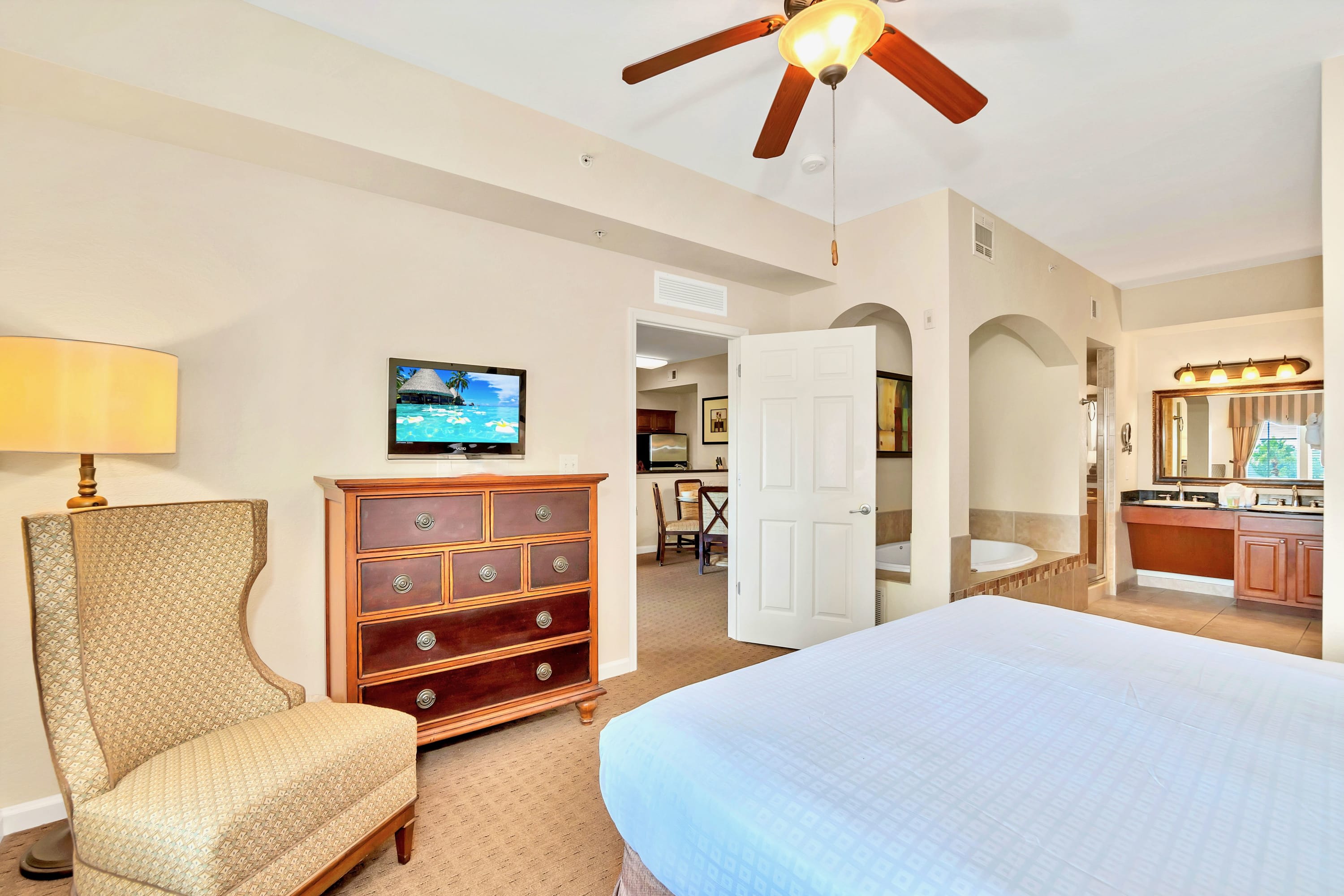 Master bedroom with a king bed, a dresser with a television, and an arched doorway leading to an en-suite bathroom with a jetted tub visible in the background.