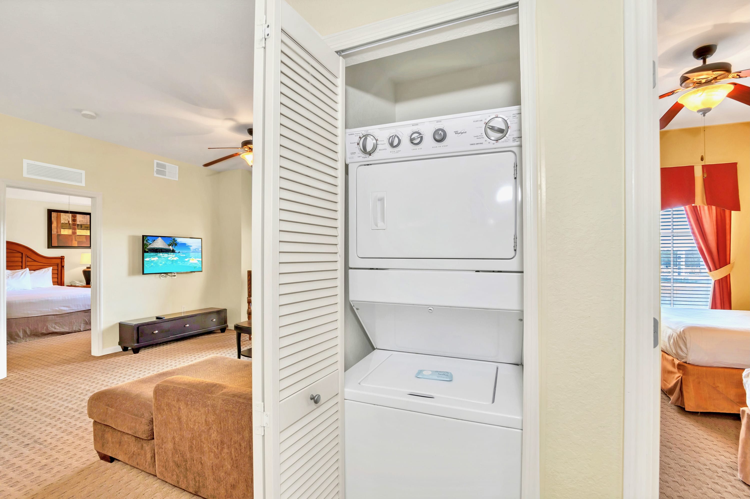 A white stacked washer and dryer unit is neatly tucked into a louvered closet, providing convenient in-unit laundry facilities. The closet is situated between two rooms, one appearing to be a living area and the other a bedroom.