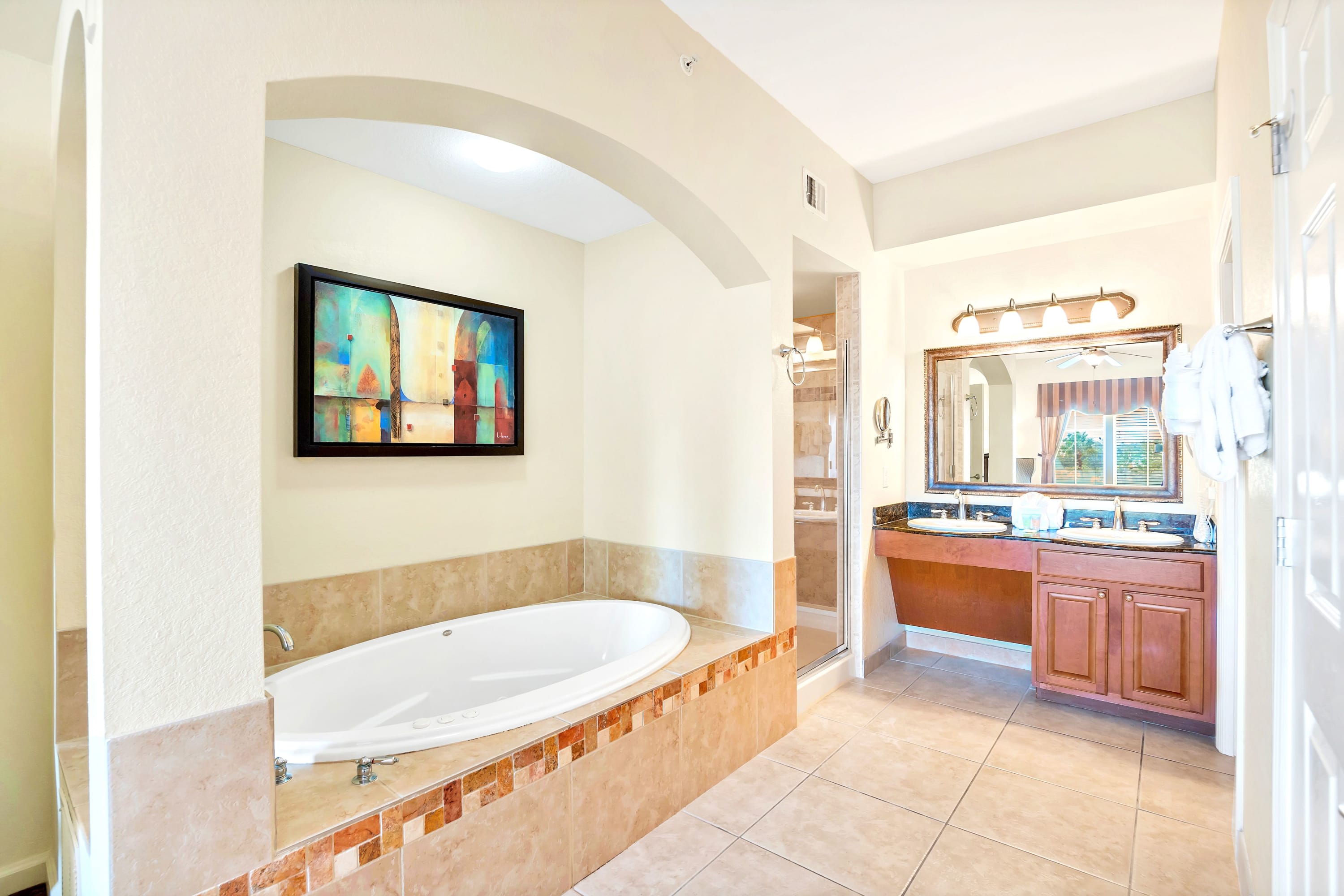 Spacious en-suite bathroom with a jetted tub, a walk-in glass shower, and a double vanity featuring dark granite countertops and a large framed mirror.