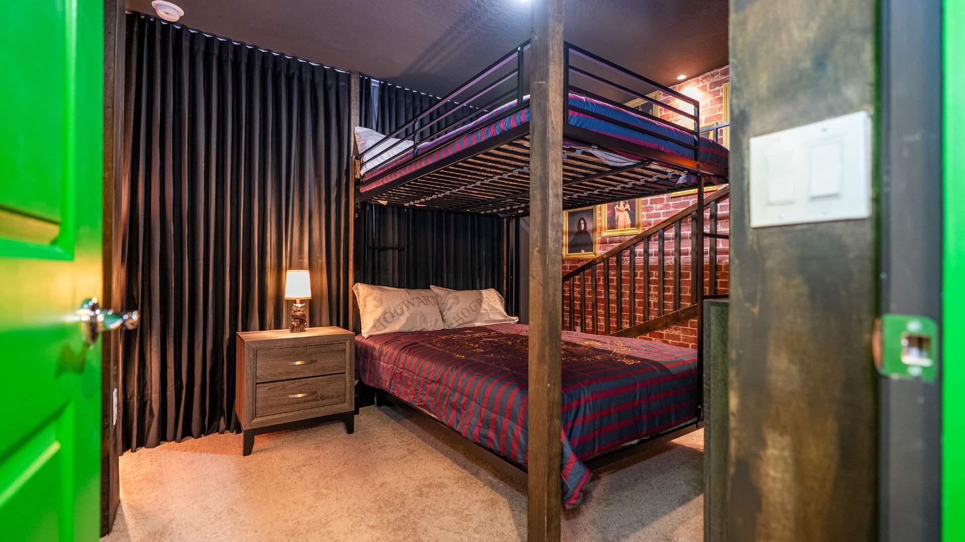 Dark-themed Harry Potter bedroom with a metal bunk bed, dark pleated curtains, a wooden nightstand with a lamp, and a brick-patterned wall.