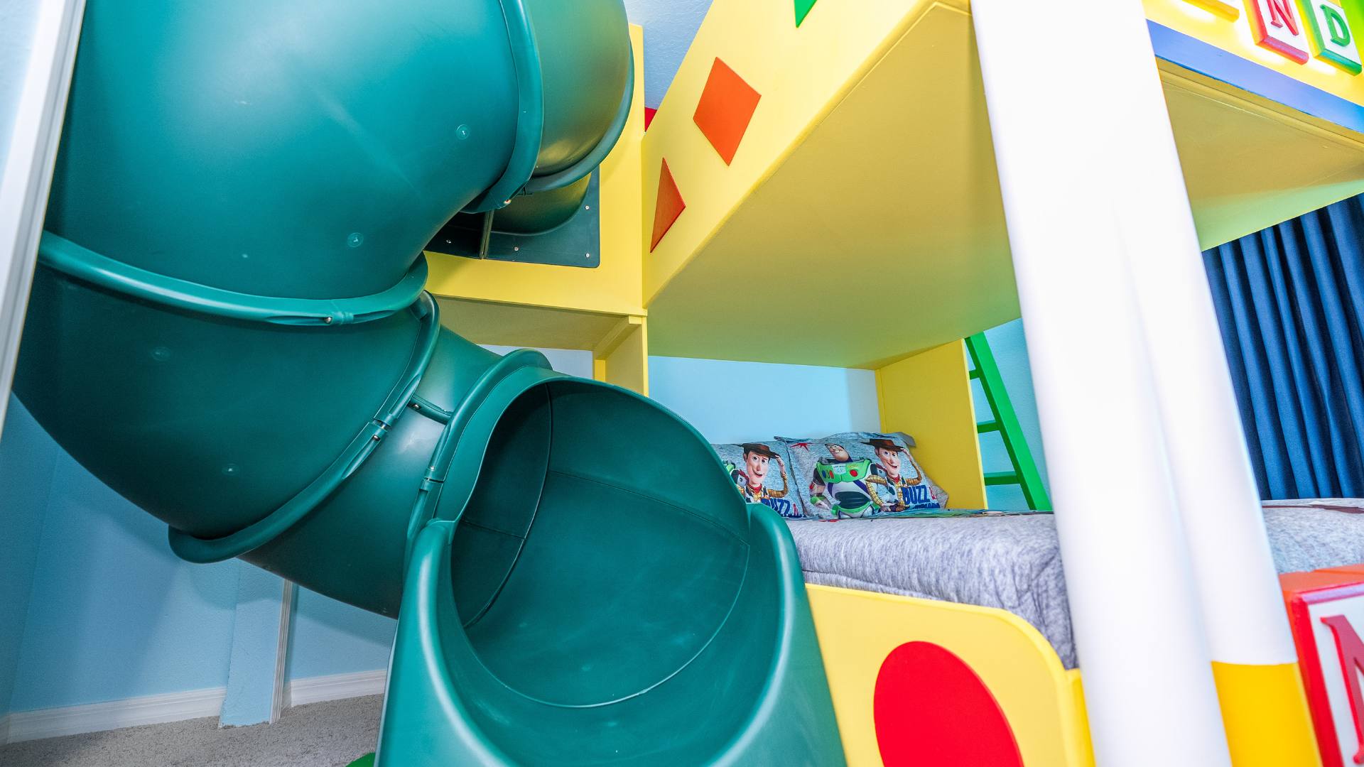 Detailed view of the green enclosed slide integrated into the colorful Toy Story themed bunk bed, with themed bedding visible below.