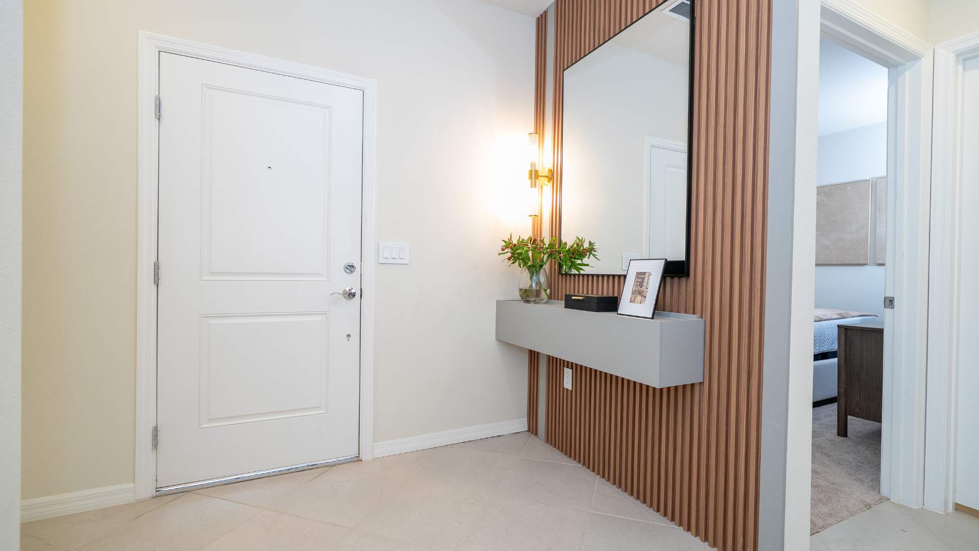 Bright foyer with a white front door, a slatted wooden accent wall, and a floating gray console table adorned with a mirror and decorative items.