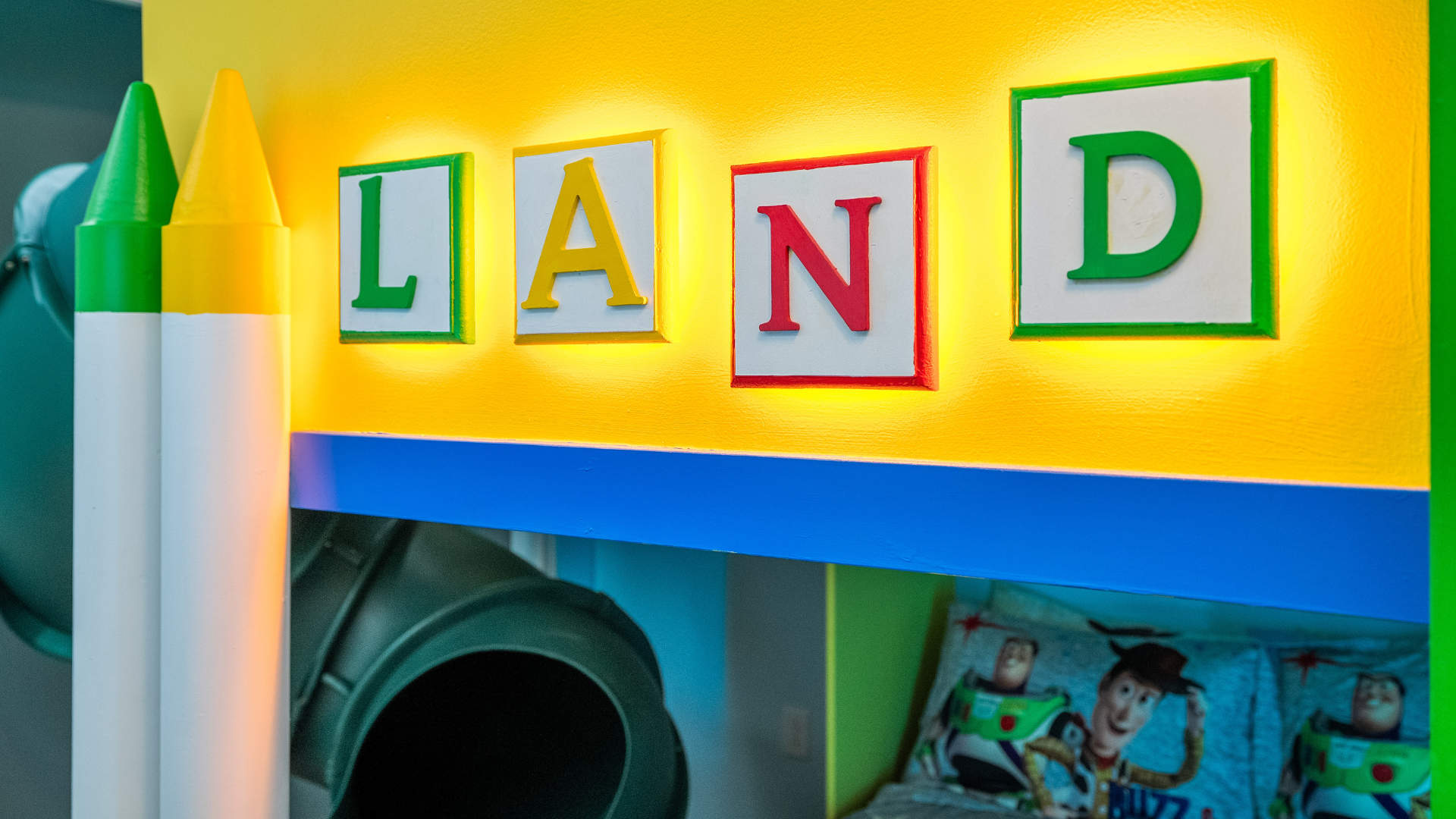 Close-up of the vibrant Toy Story themed bunk bed, featuring illuminated "LAND" letters, colorful crayon decorations, and a glimpse of the green slide.