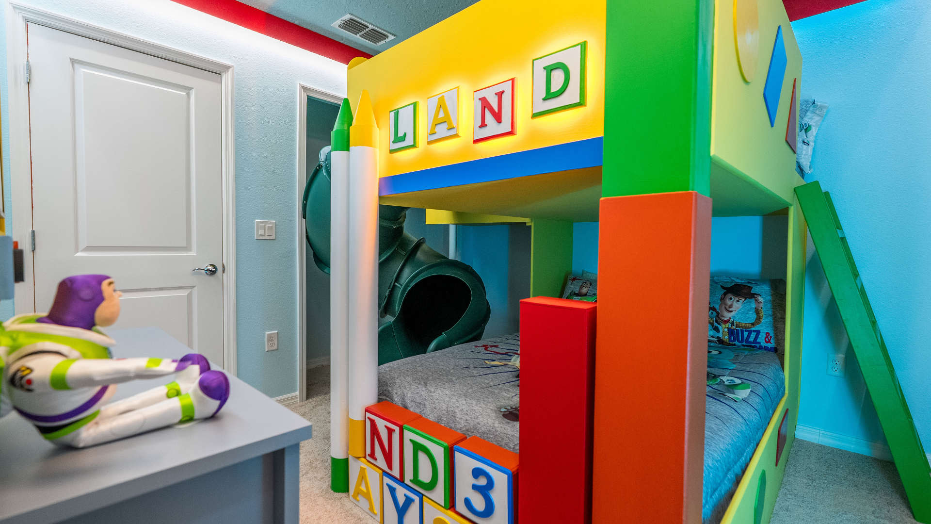 Vibrant Toy Story themed bedroom featuring a colorful bunk bed with a built-in slide, playful block decorations, and a Buzz Lightyear figure on a desk.