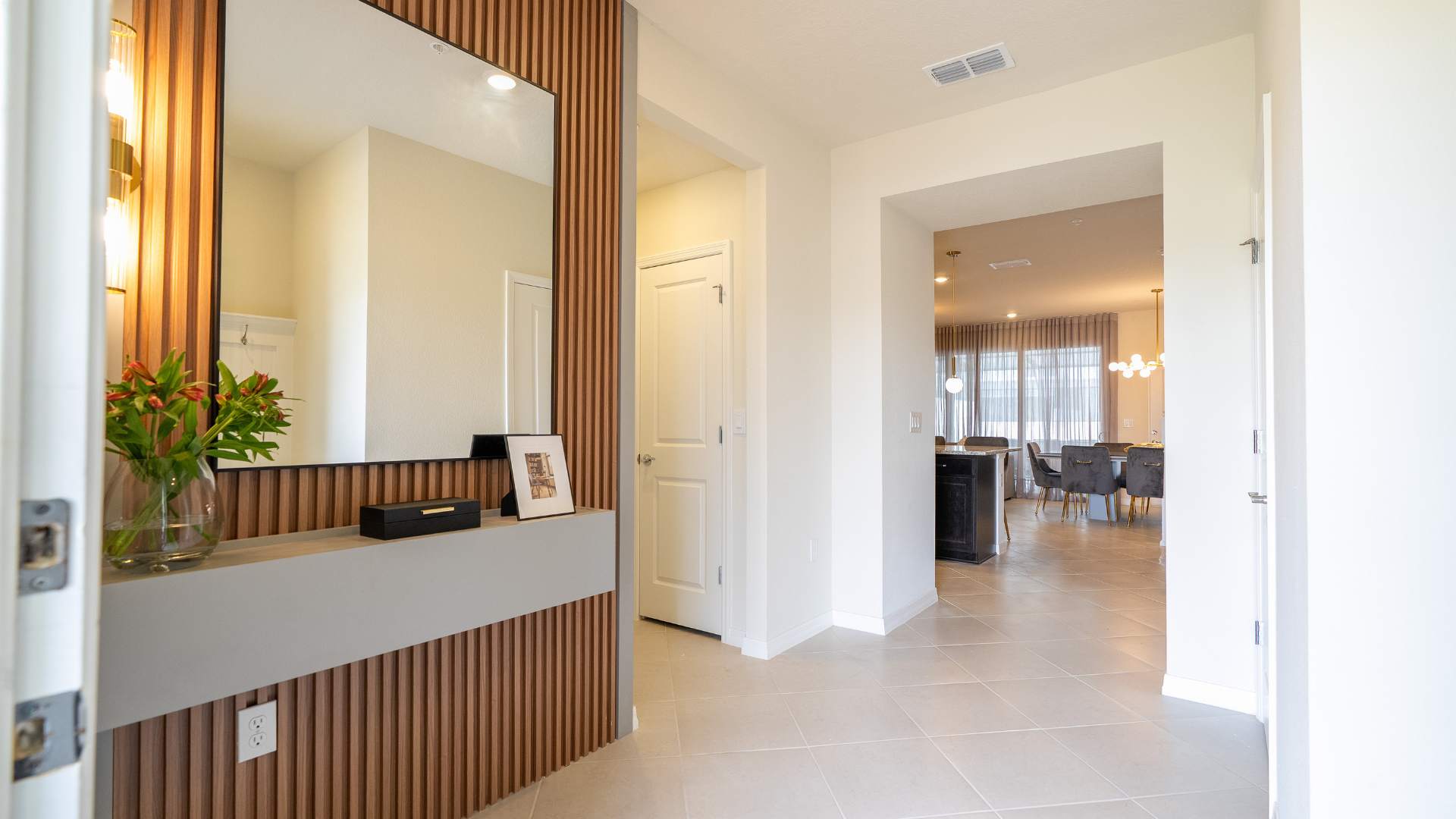 Modern foyer featuring a large mirror and a floating gray console table against a slatted wooden accent wall, with a glimpse into a dining area beyond.