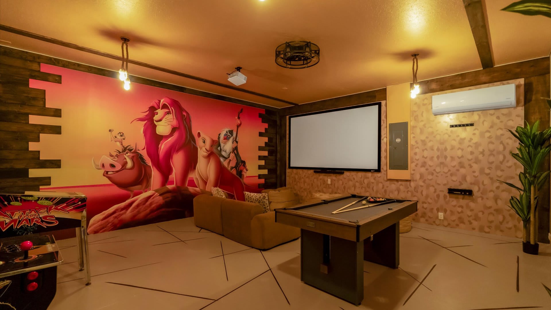 Themed game room with a large projection screen, a brown sofa, and a pool table. One wall features a vibrant 'Lion King' mural, while the ceiling and other walls are painted in warm tones with wood accents.
