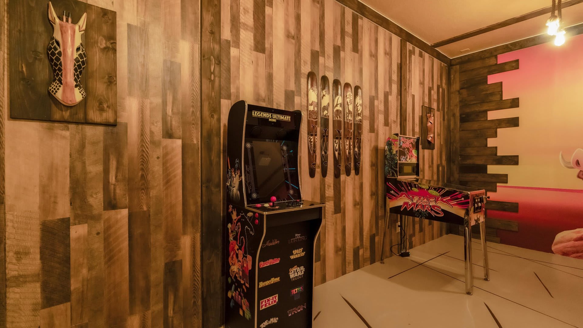 A game room with wood-paneled walls features a "Legends Ultimate" arcade machine and a "Star Wars" pinball machine, illuminated by warm overhead lighting. Decorative wooden skis are mounted on the wall.