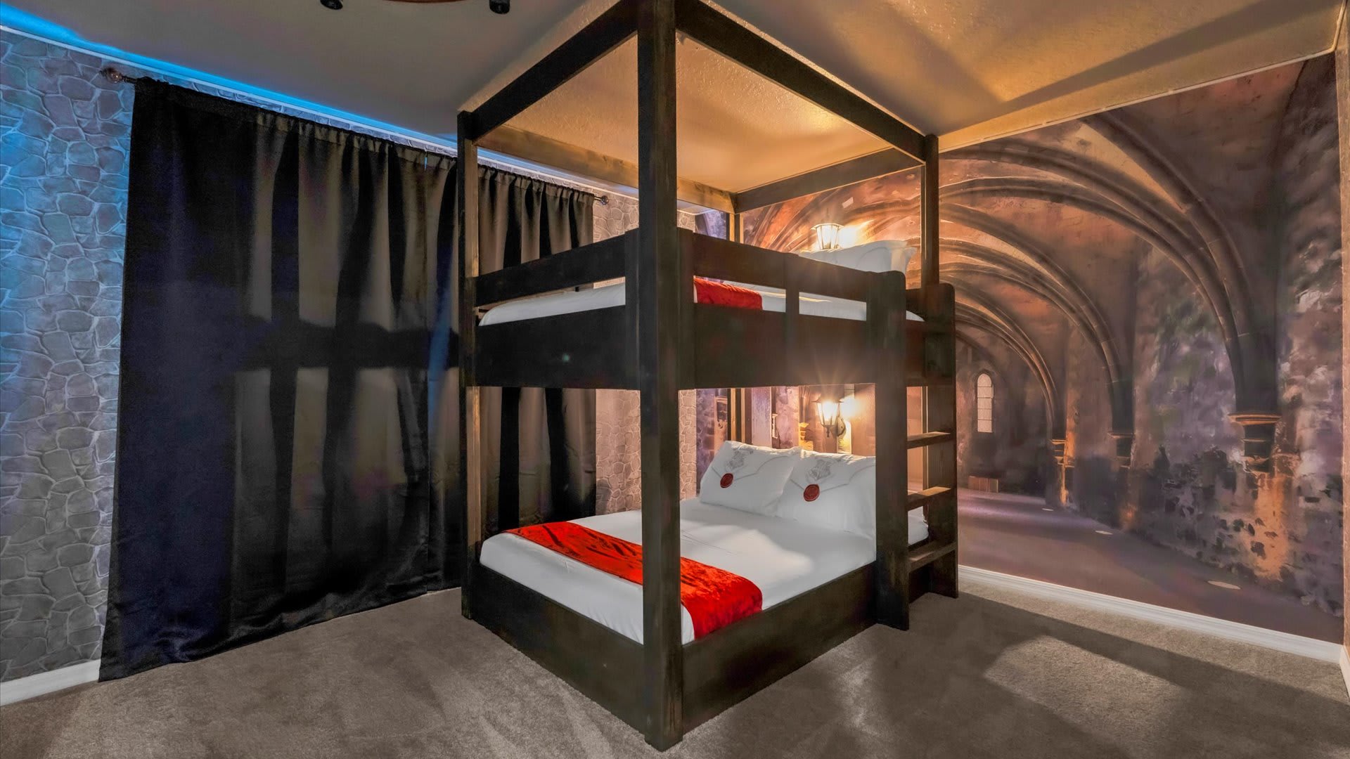 A wide shot of the Harry Potter-themed bedroom, featuring a dark wooden bunk bed with red bedding. The walls are decorated with a stone archway mural and a textured stone-like wallpaper, with dark curtains on the left.