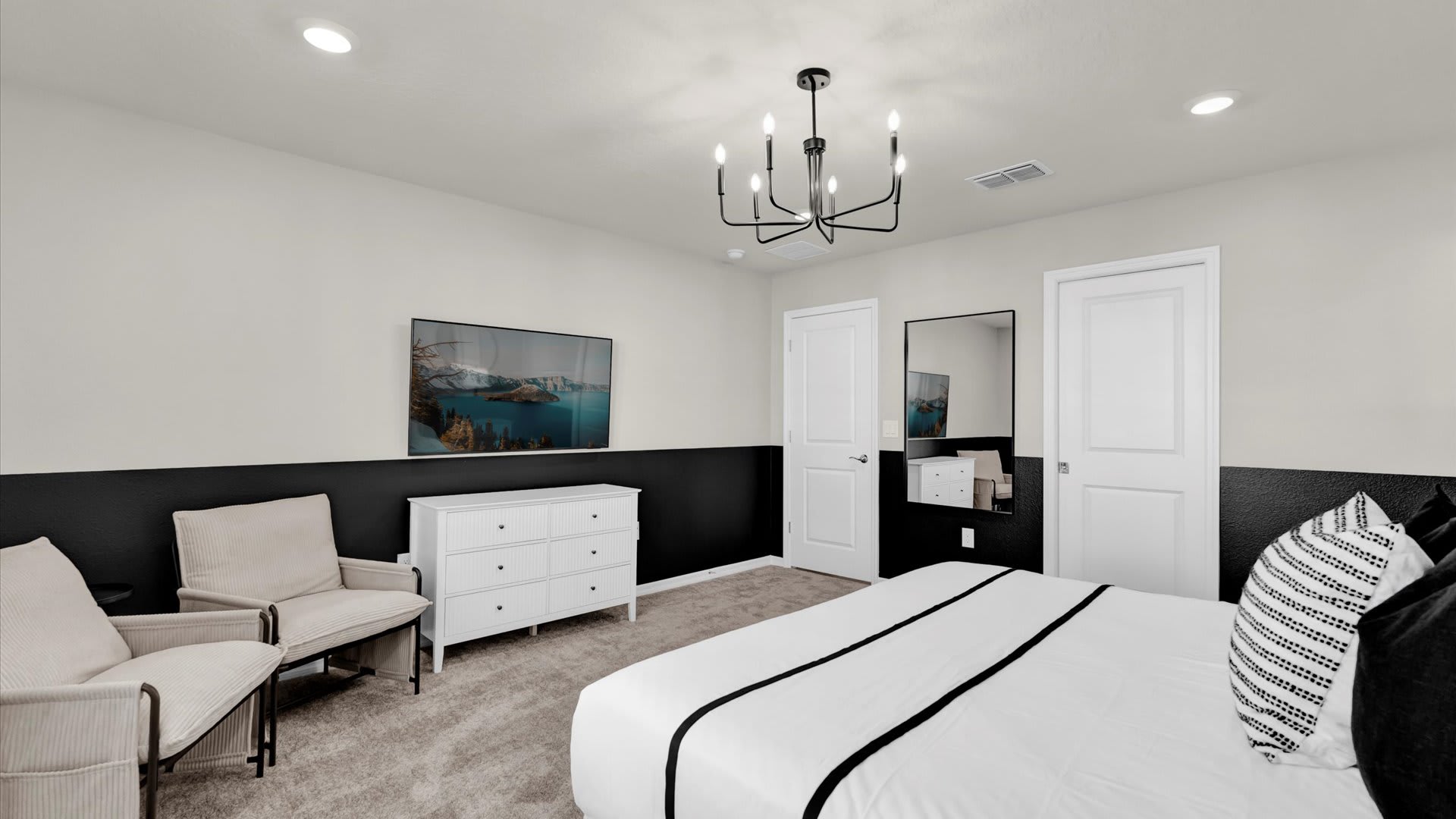 Another view of the master bedroom, showcasing a white dresser with a wall-mounted TV above it on the black accent wall. Two white doors are visible, along with a full-length mirror leaning against the wall.