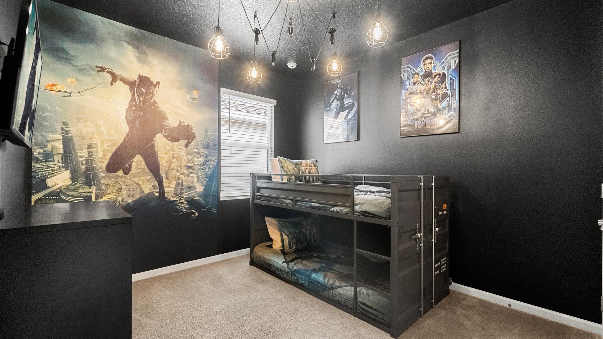 Dark-themed kids' bedroom featuring a large Black Panther mural on one wall, a black metal bunk bed designed like a shipping container, and industrial-style pendant lighting.