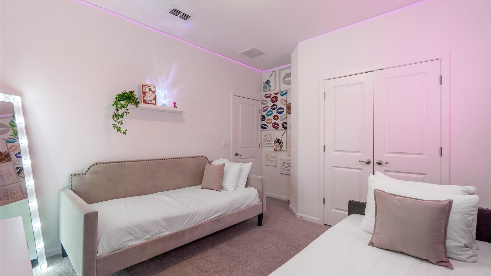 Vibrant pink-themed bedroom with a tufted daybed, a full-length lighted mirror, and a gallery wall featuring various lip art prints, creating a playful and stylish atmosphere.