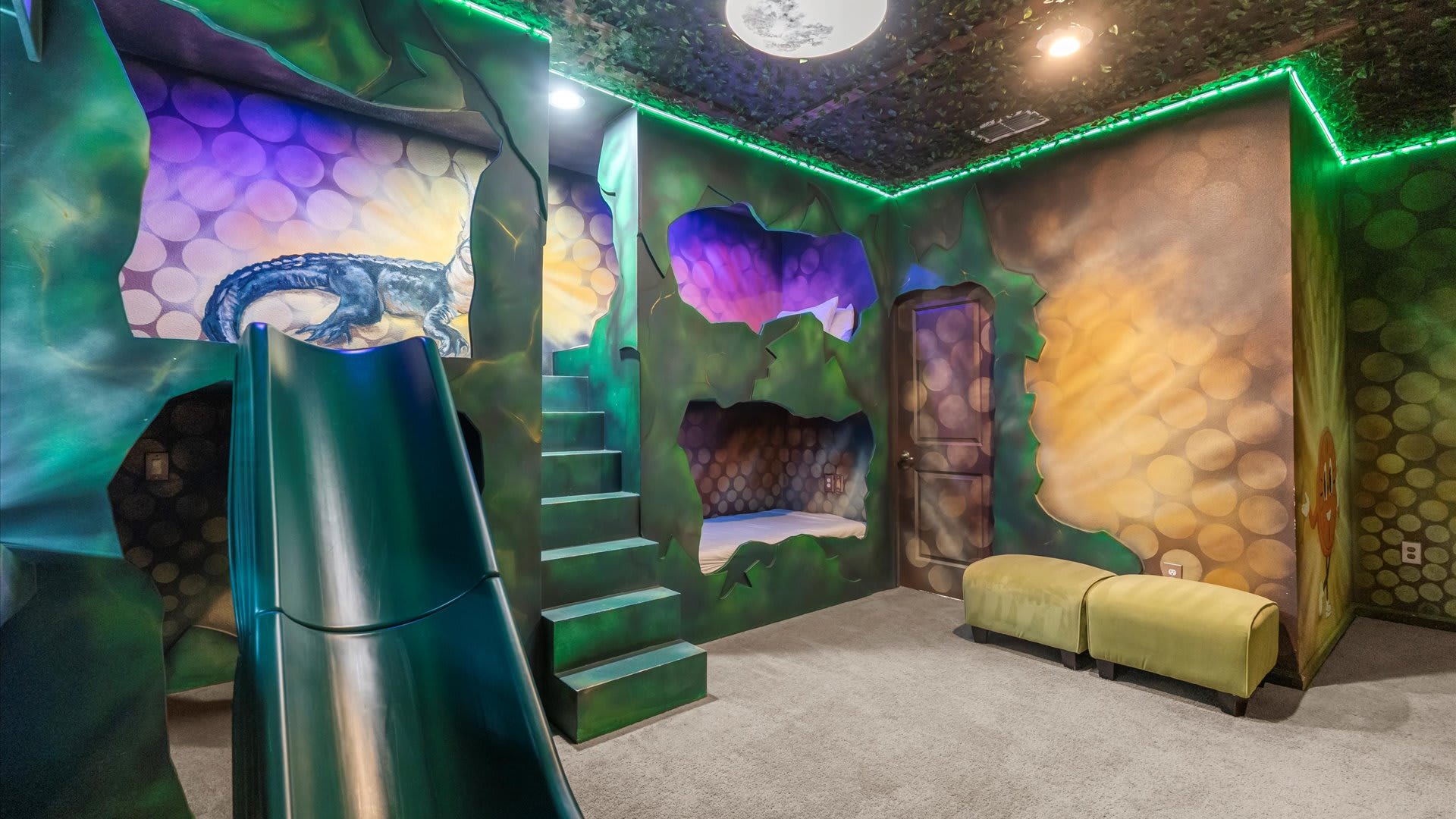 Another angle of the jungle-themed bedroom, highlighting the built-in bunk beds with steps leading to the upper bunk and a green slide. The walls are intricately painted with cave-like designs and foliage.