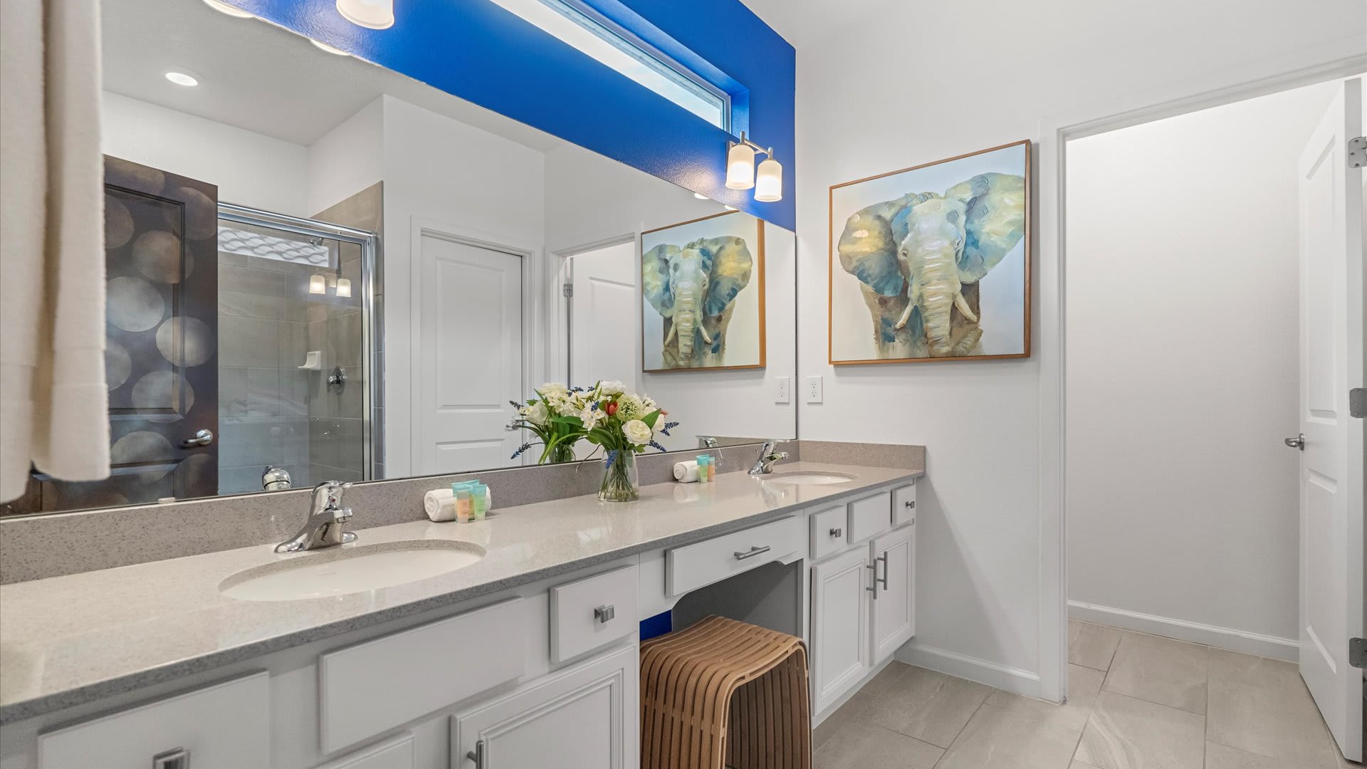 Spacious bathroom with a double vanity featuring light gray countertops, white cabinets, and a large mirror. A vibrant blue accent wall above the mirror adds a pop of color.