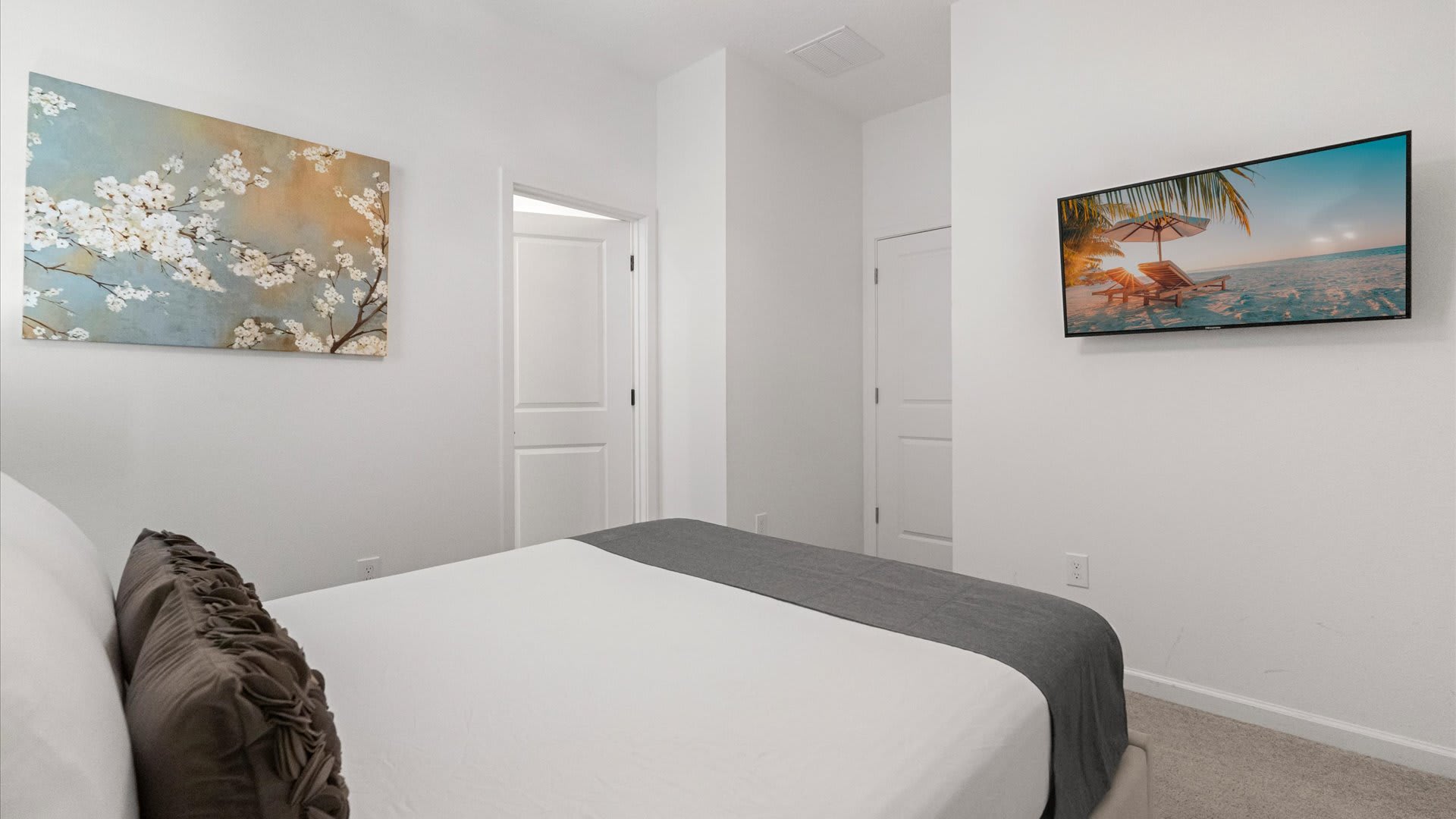 View of bedroom-3 showing a wall-mounted TV, a large abstract floral painting, and a bed with white and gray bedding.