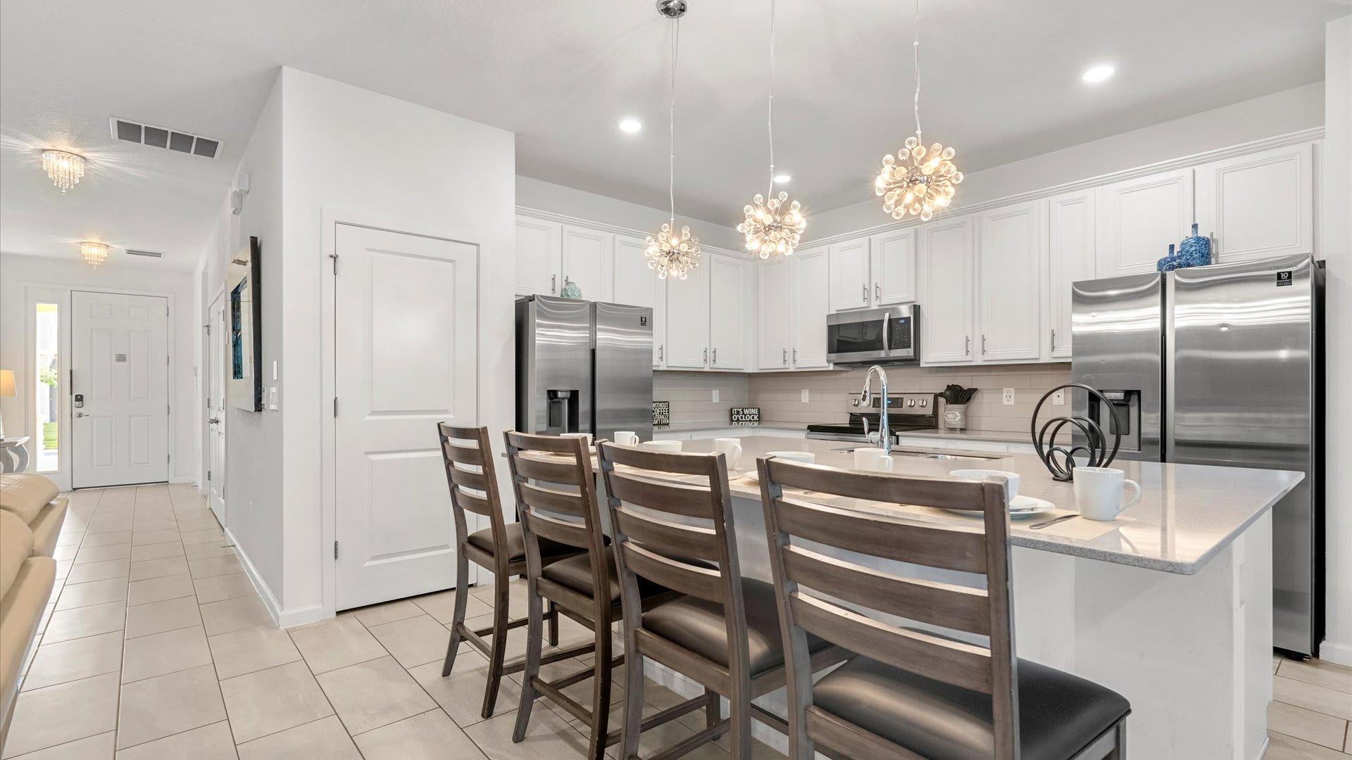 A contemporary kitchen with white shaker cabinets, stainless steel appliances, and a large island with bar seating, illuminated by three unique pendant lights.