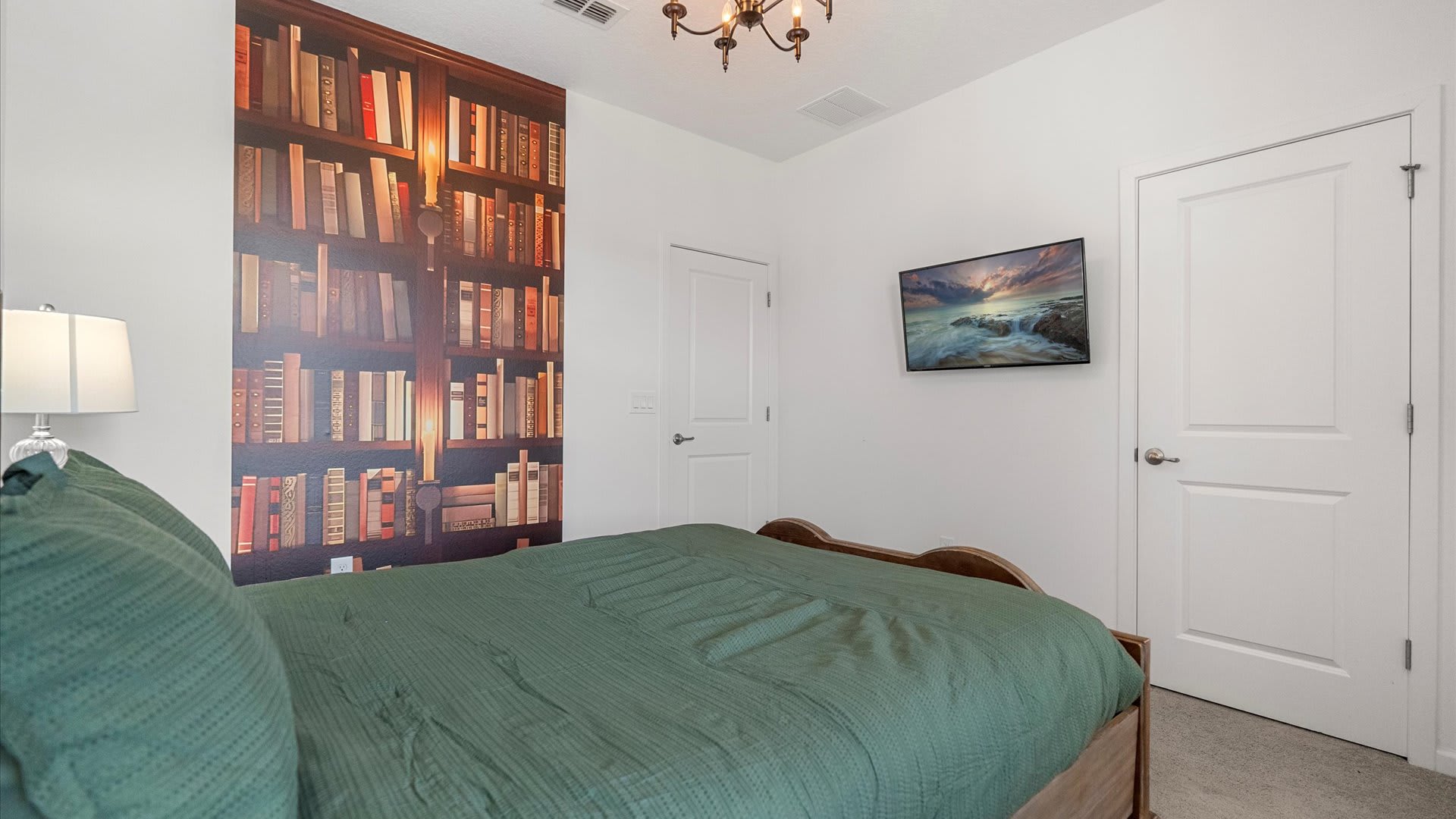 View of the Harry Potter themed bedroom showing a large bookshelf mural on one wall, a dark wood bed with green bedding, and a wall-mounted TV.