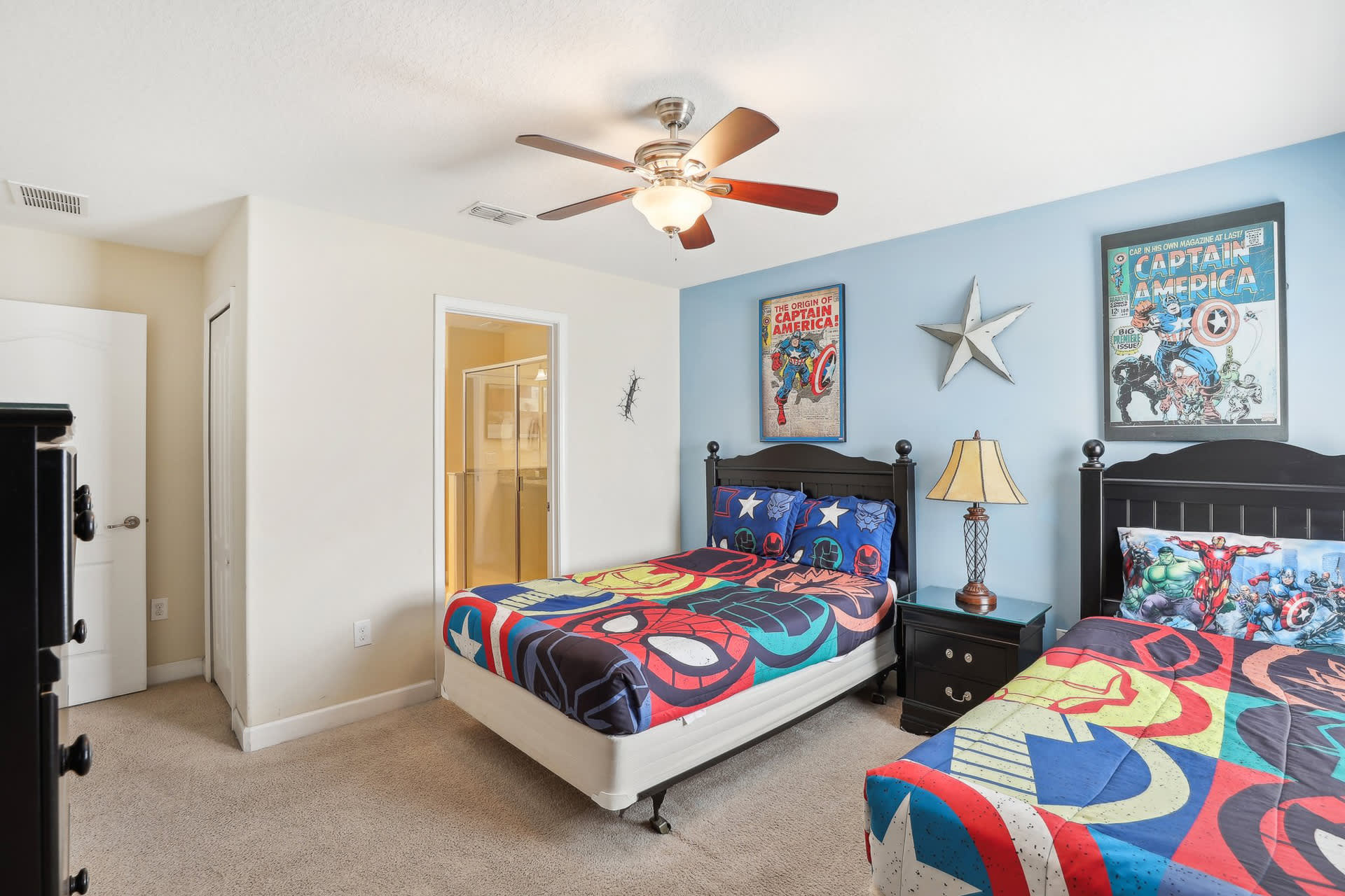 Kids' themed bedroom with two black beds featuring Marvel superhero bedding, a light blue accent wall with vintage Captain America posters, and a ceiling fan.
