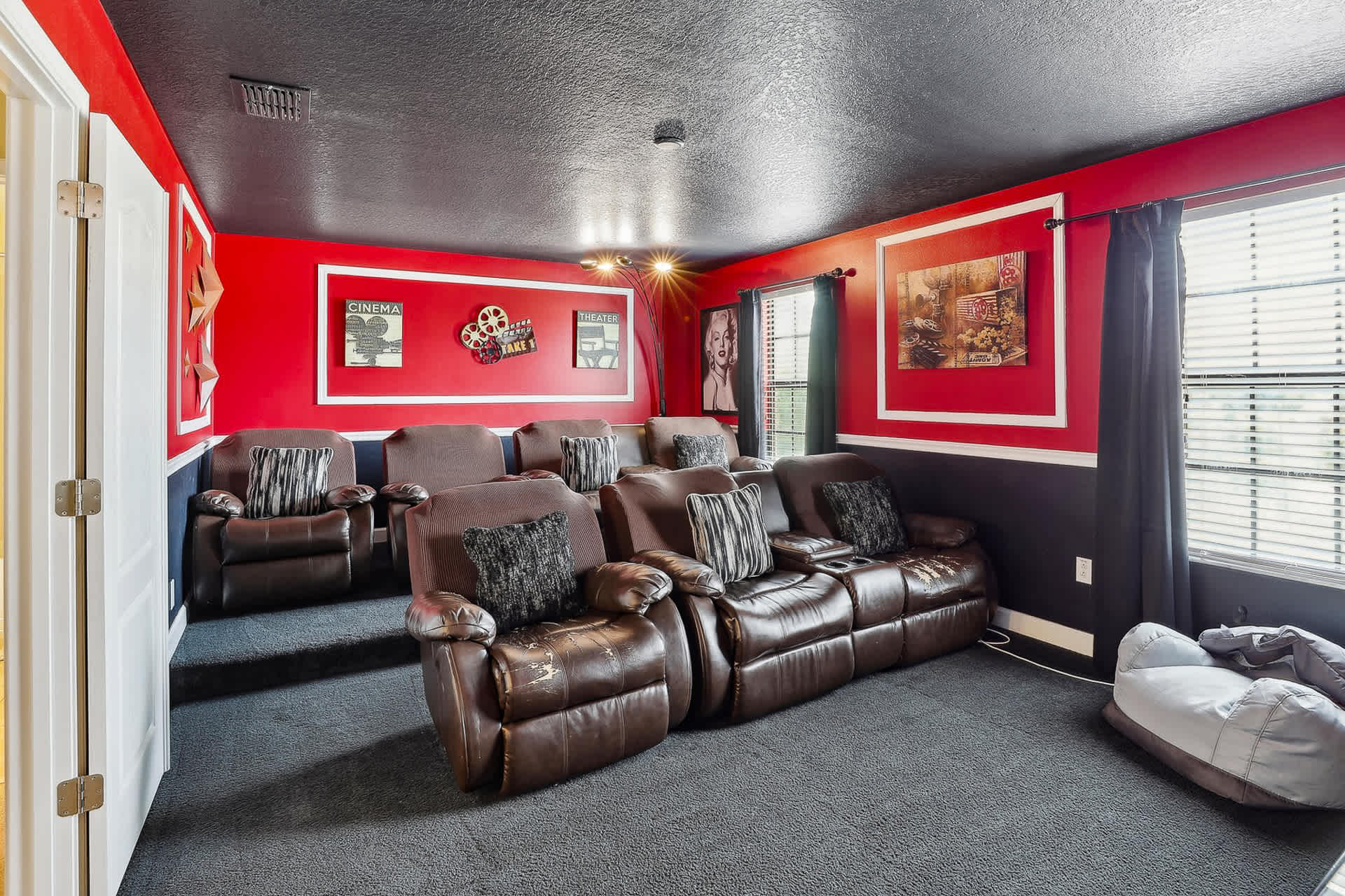 Dedicated media room with multiple rows of plush brown reclining seats, offering a comfortable viewing experience. The room features red and black walls, dark carpet, and movie-themed decor, including framed posters.