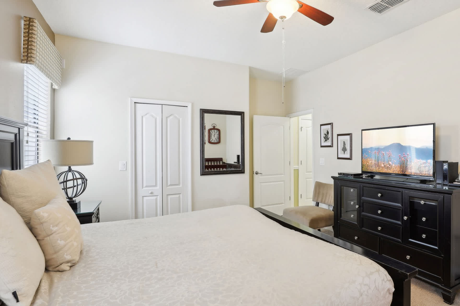 View of the master bedroom from a different angle, showing the dark wood bed frame, a dresser with a TV, and a full-length mirror. A closet and a doorway to an en-suite bathroom are also visible.