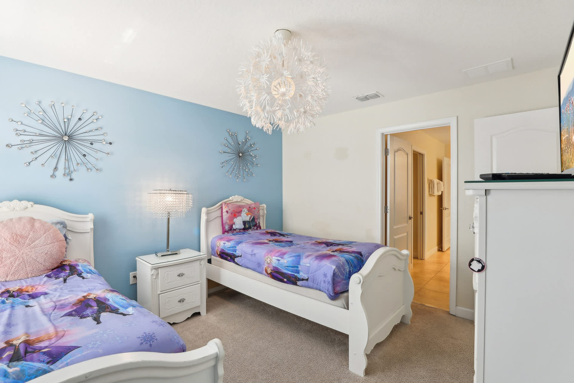 Kids' themed bedroom with two white twin beds featuring 'Frozen' bedding, a light blue accent wall adorned with starburst decor, and a unique white spiky chandelier.