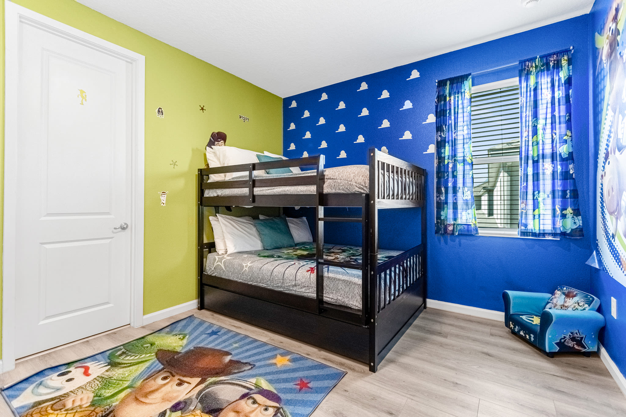 Playful Toy Story-themed bedroom with a dark wood bunk bed, lime green and blue walls, and a window with blue curtains. A Toy Story rug covers the light wood-look floor.