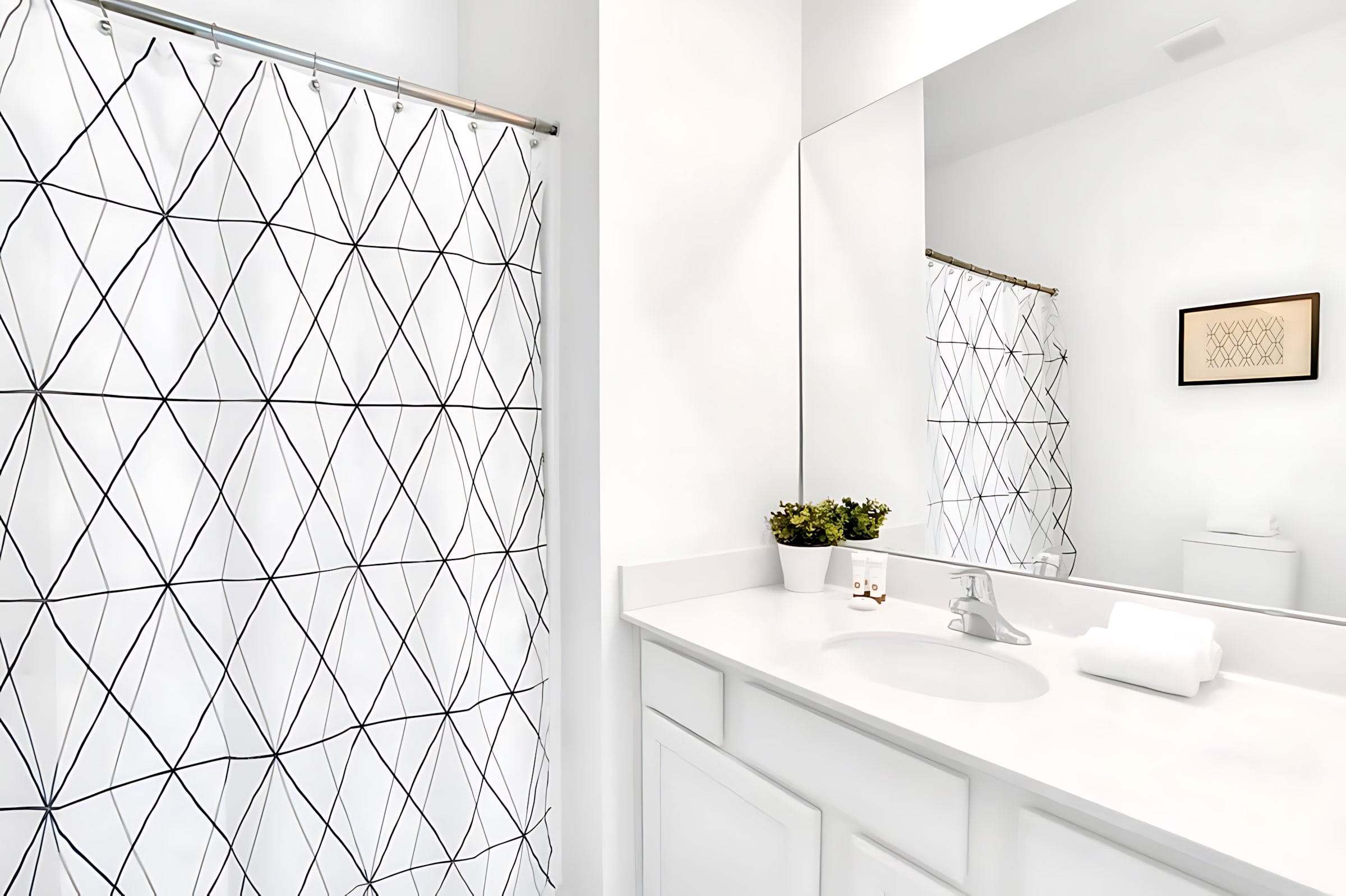 Modern white bathroom with a single vanity, large mirror, toilet, and a shower/tub combo featuring a black and white geometric patterned shower curtain.