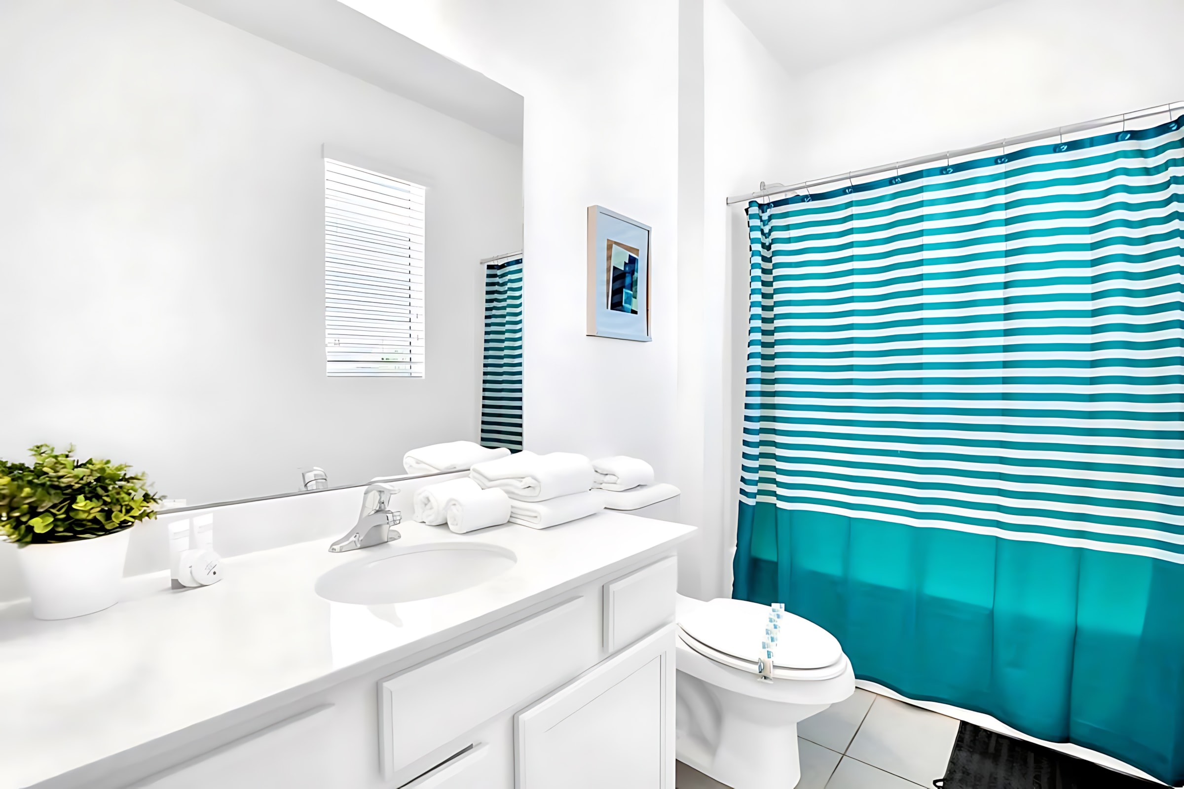 Contemporary bathroom with a white single vanity, large mirror, toilet, and a shower/tub combo featuring a vibrant teal and white striped shower curtain.
