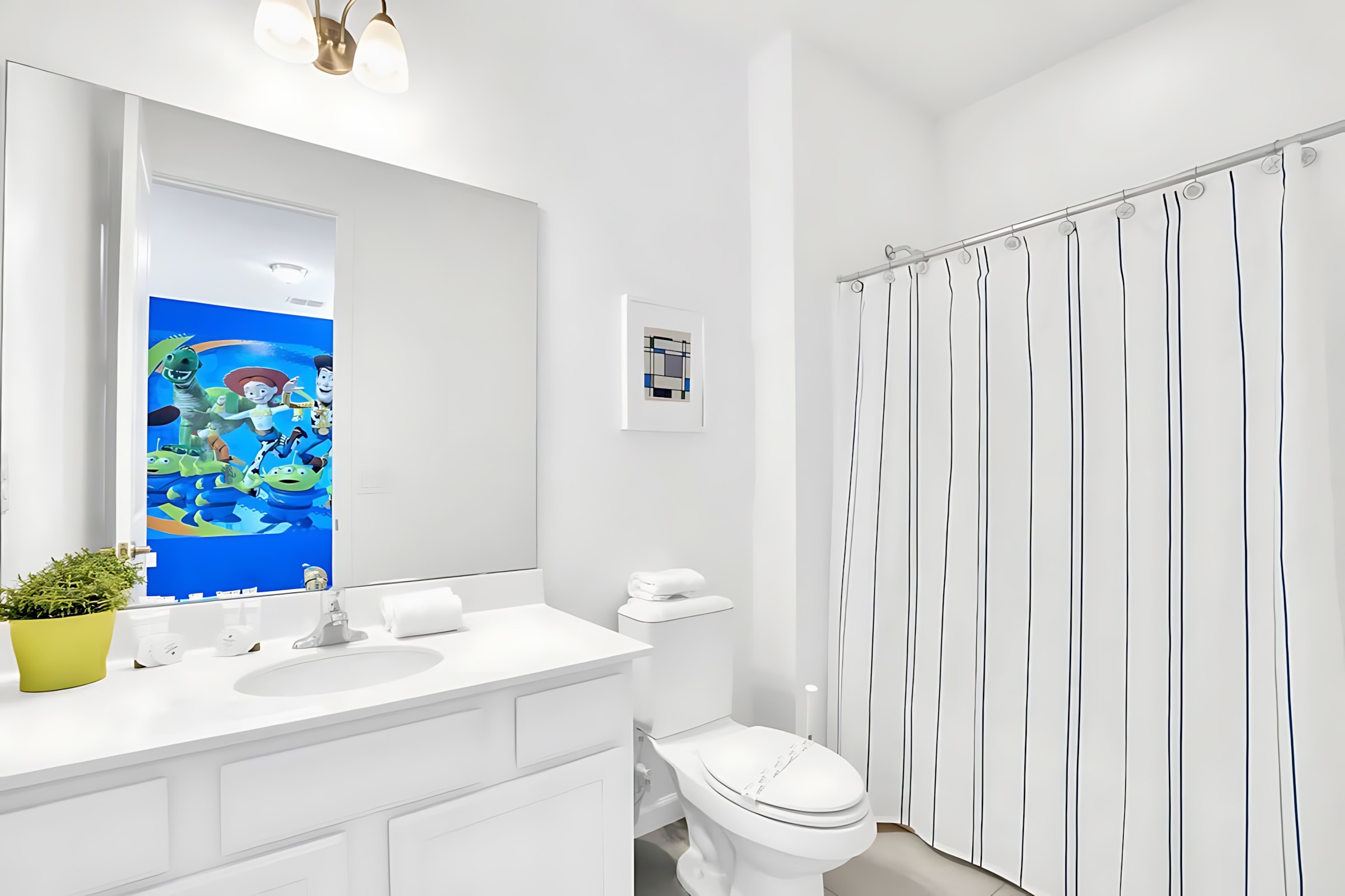 Clean white bathroom with a single vanity, toilet, and a shower with a blue and white striped curtain. The mirror reflects the vibrant Toy Story-themed bedroom.
